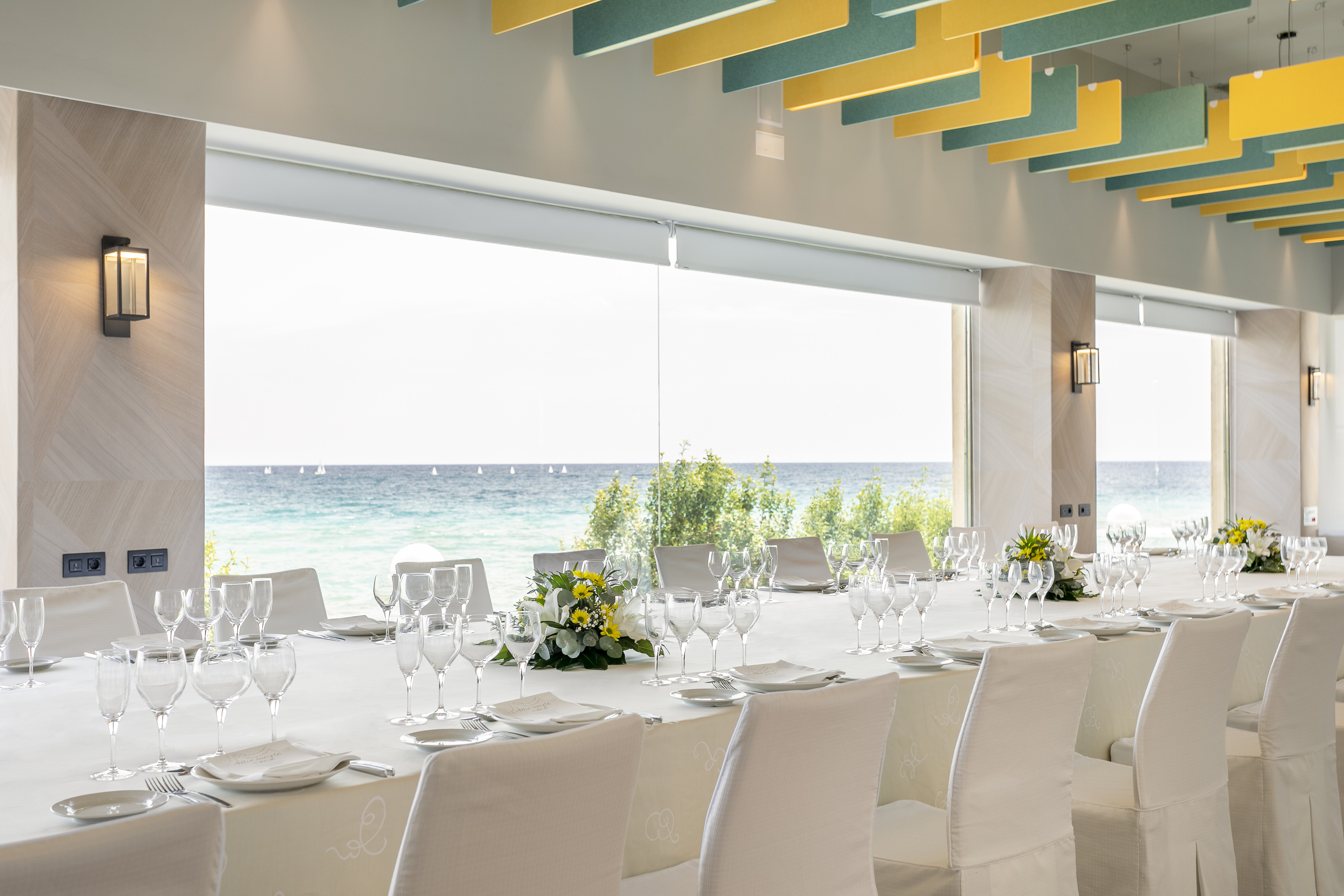 Modern oceanfront banquet room, long table set with glassware & flowers.