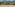 Empty outdoor beach volleyball court on sand with yellow net, surrounded by trees.