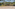 Empty outdoor beach volleyball court on sand with yellow net, surrounded by trees.
