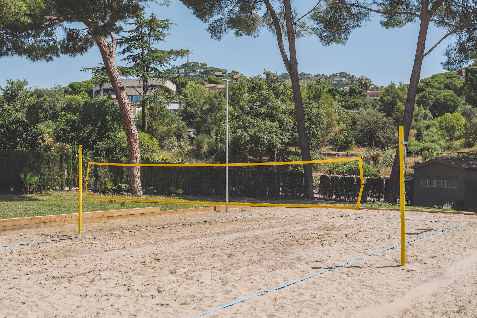 Empty outdoor beach volleyball court on sand with yellow net, surrounded by trees.