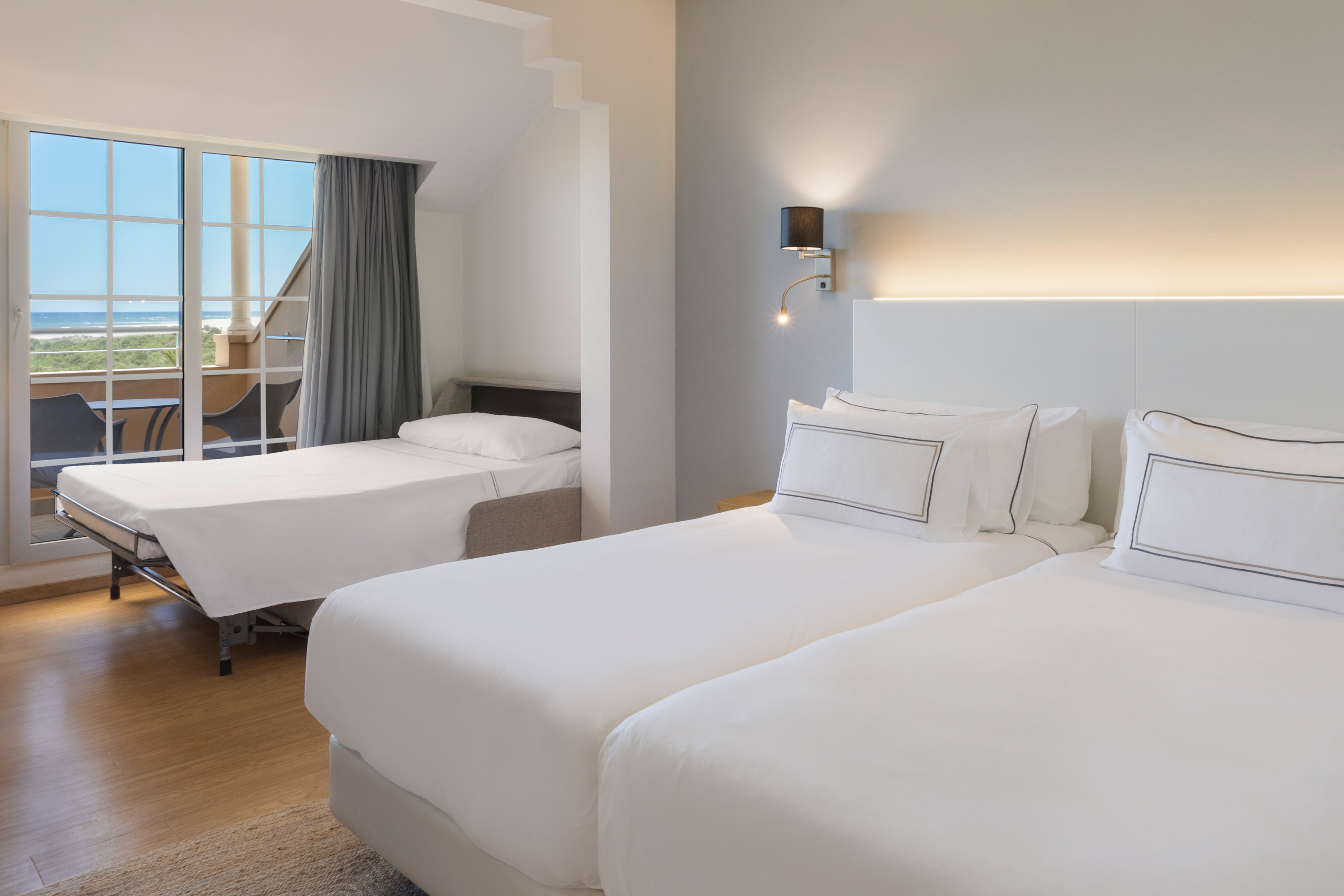 Hotel room with twin beds, rollaway bed, and ocean view balcony.