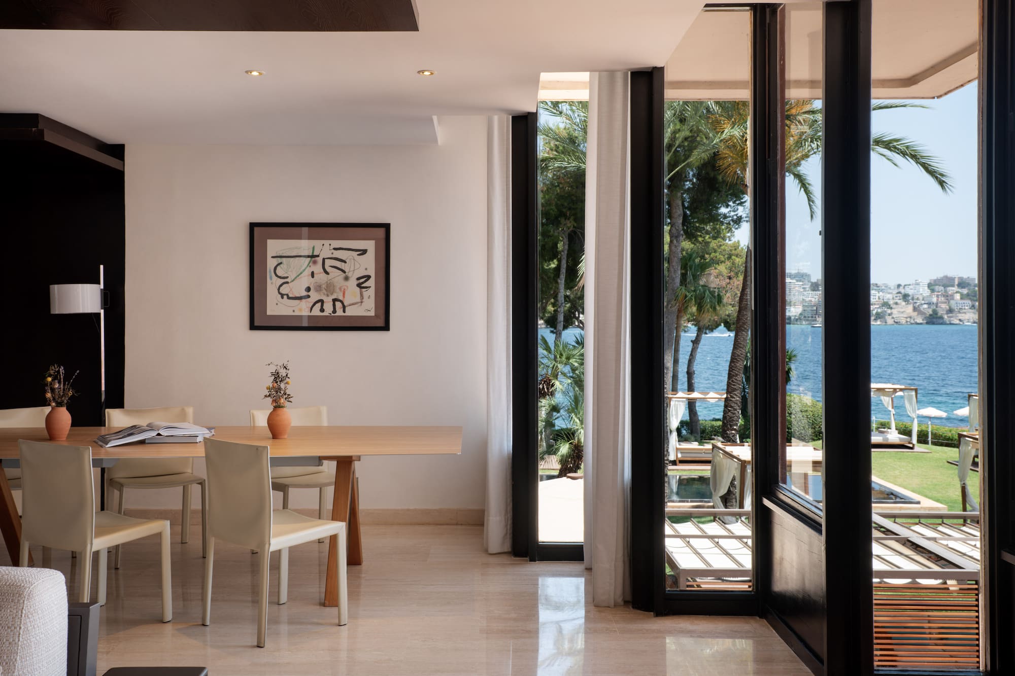 Modern dining room with ocean view, palm trees, and outdoor lounge area.