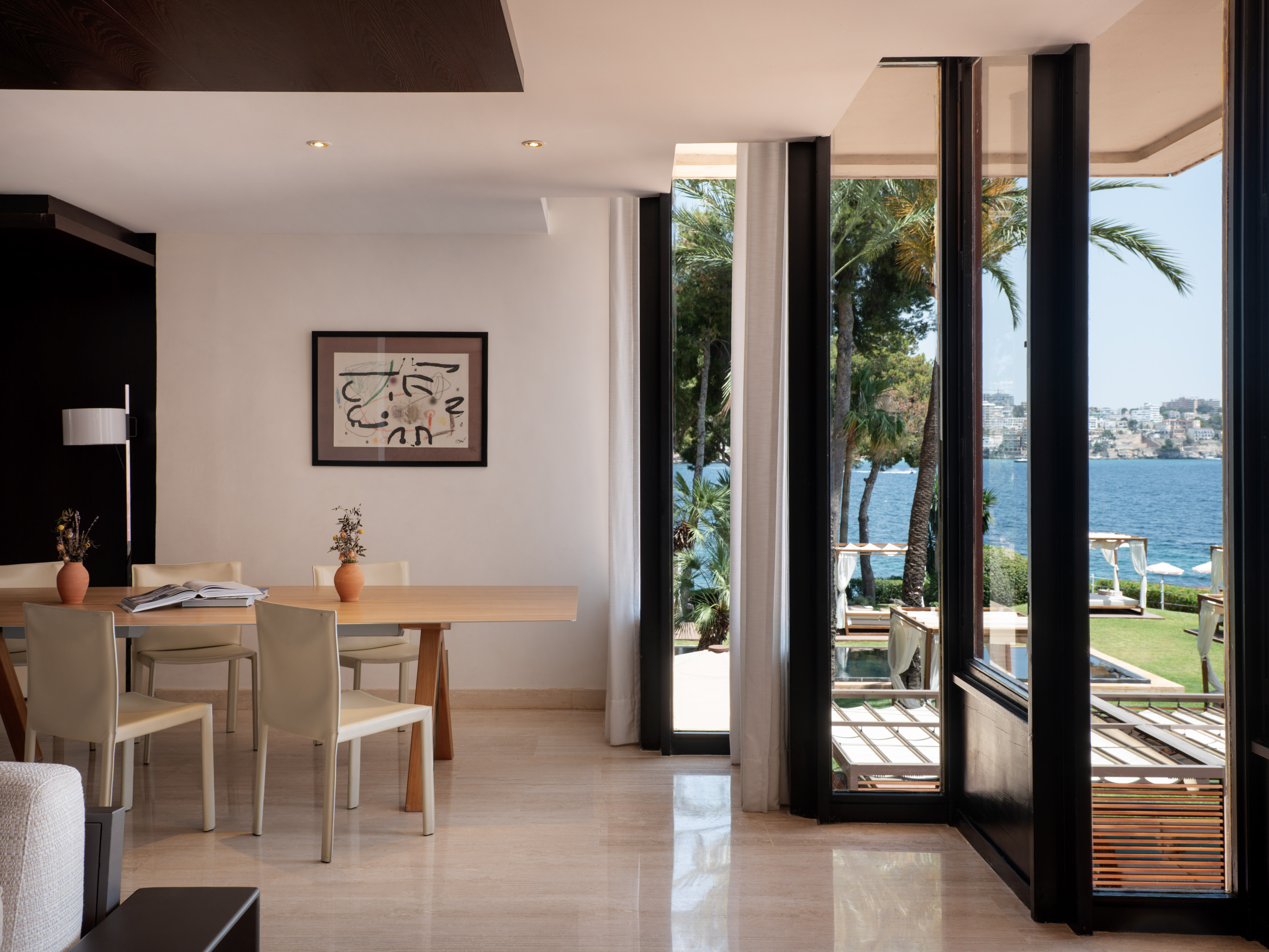 Modern dining room with ocean view, palm trees, and outdoor lounge area.