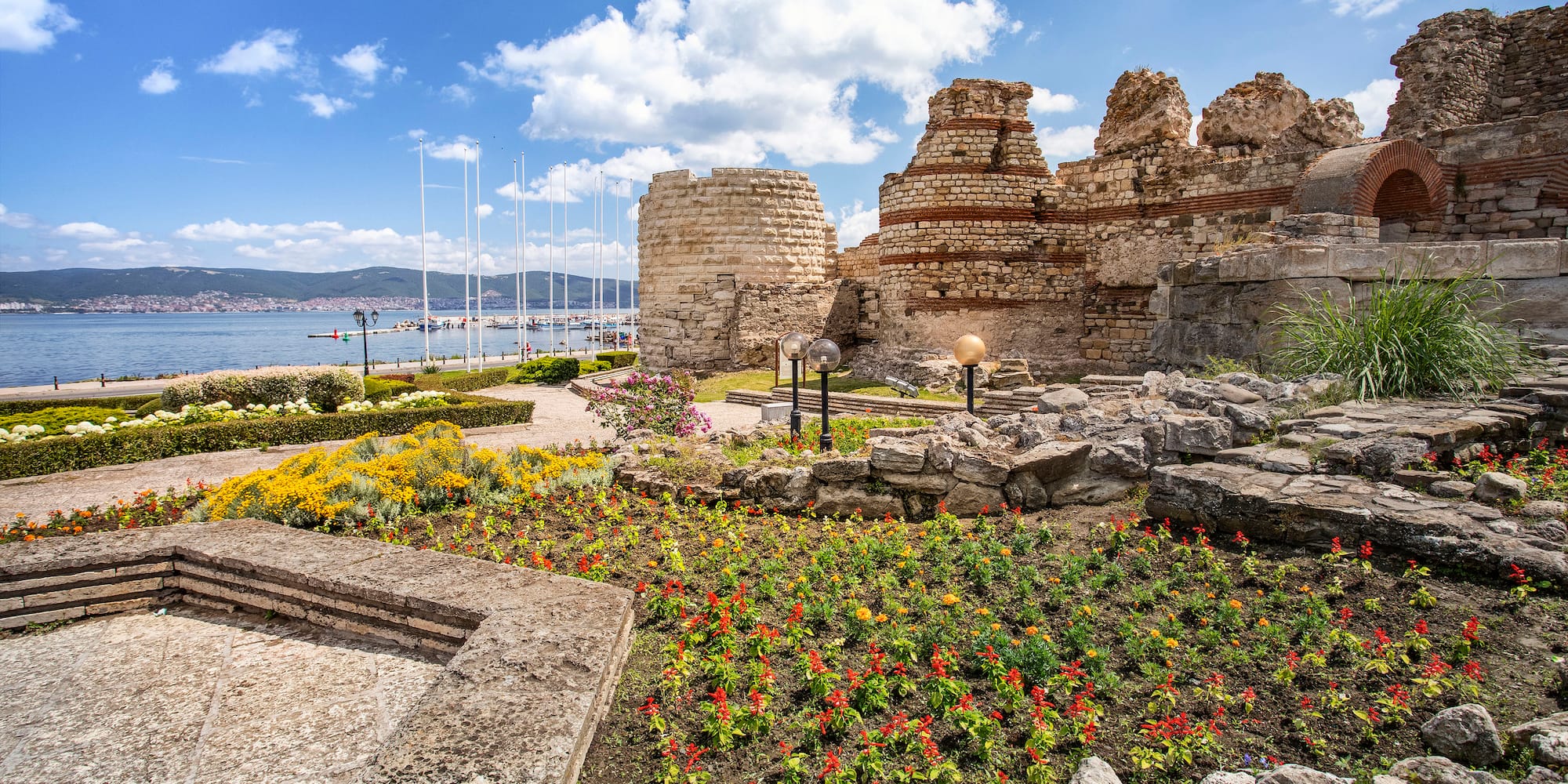 a stone ruins with flowers and plants by water