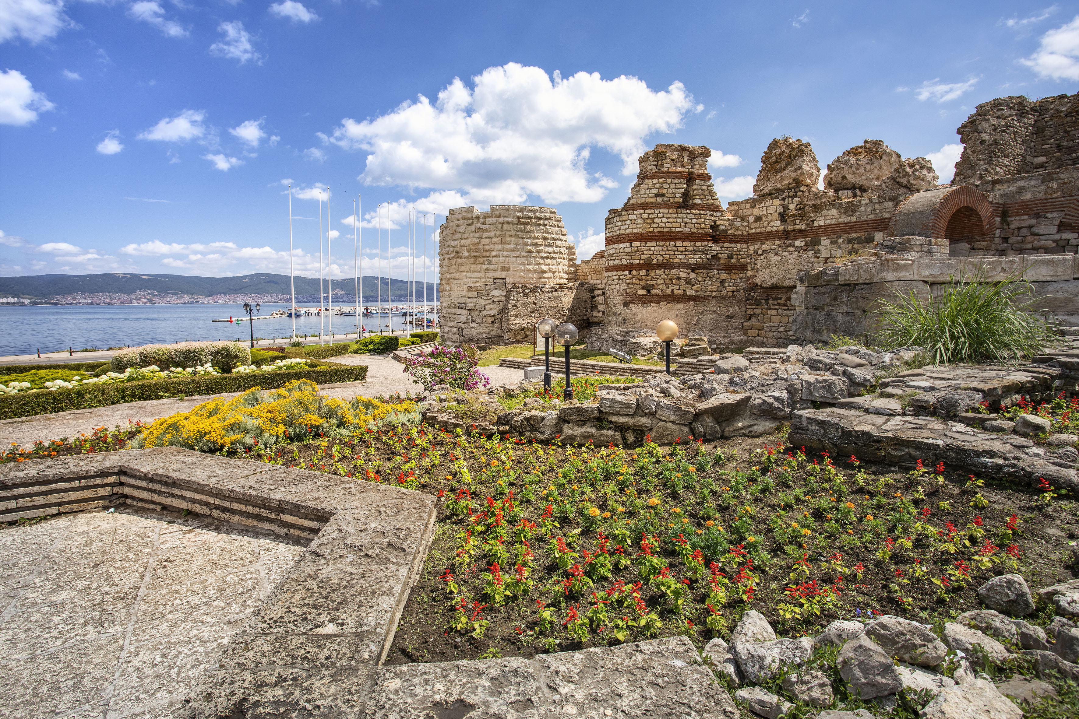 a stone ruins with flowers and plants by water