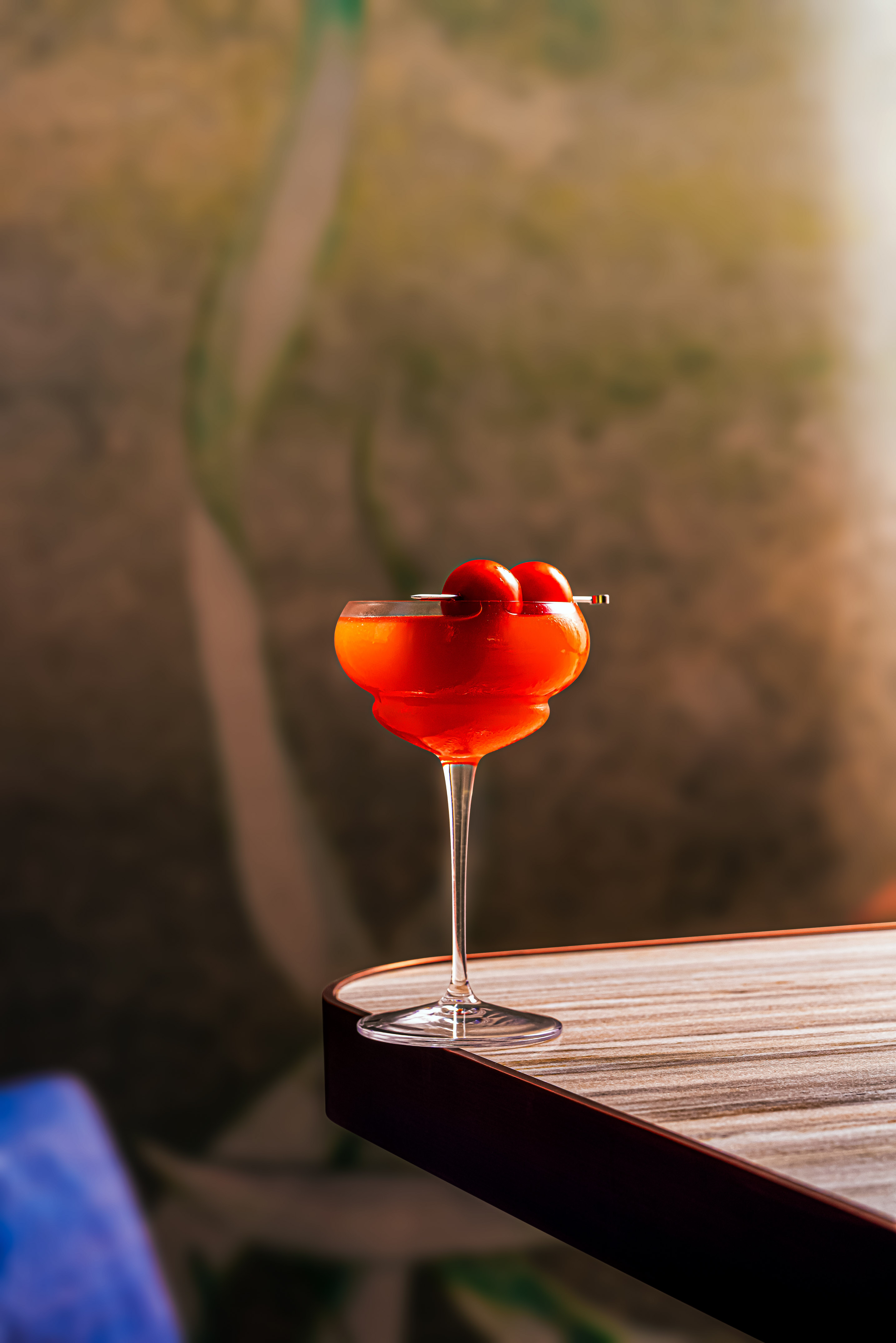 Cóctel rojo intenso en copa, con dos cerezas, sobre mesa de madera.