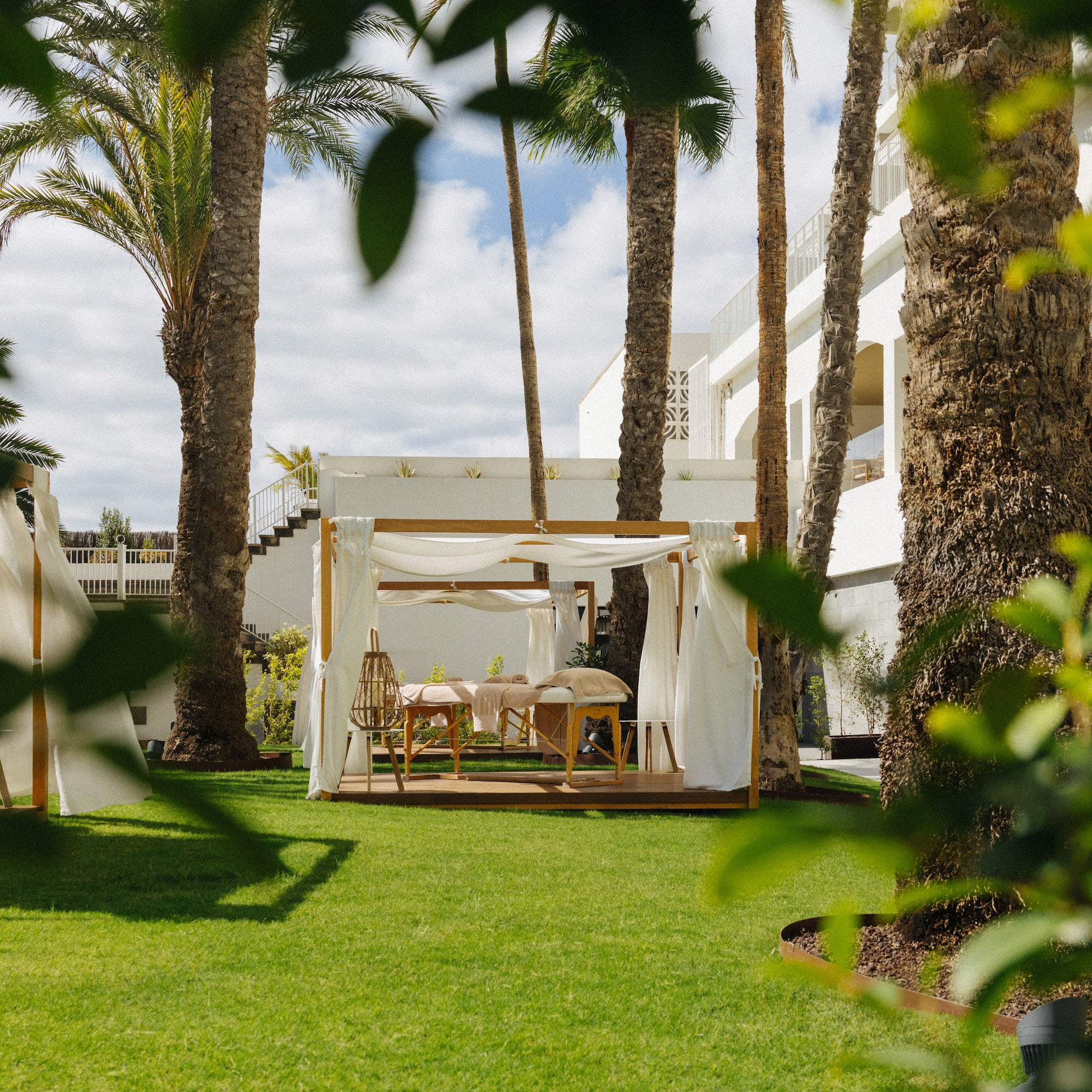 Outdoor spa cabana with massage tables, palm trees, and resort garden.