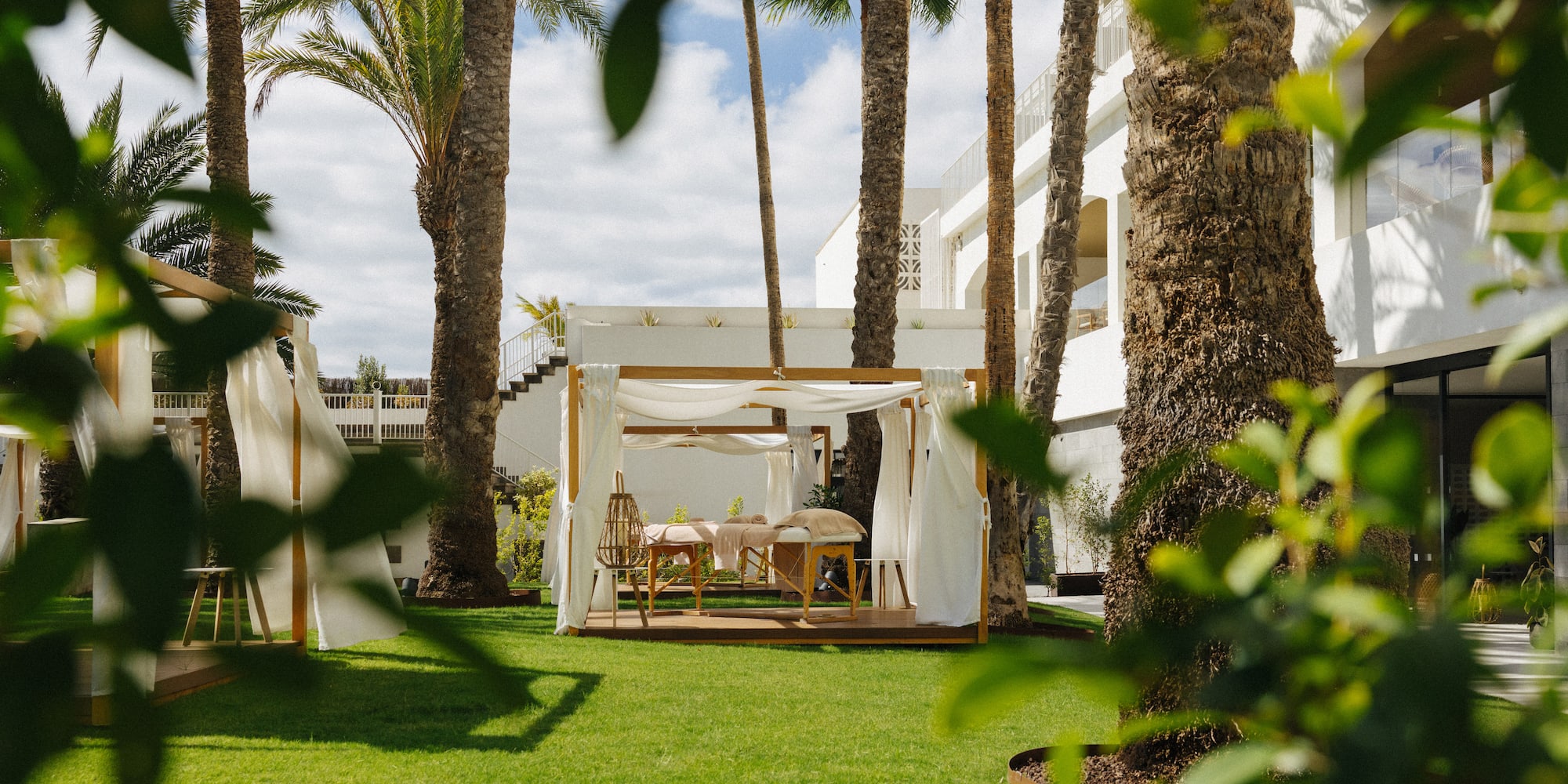 Outdoor spa cabana with massage tables, palm trees, and resort garden.
