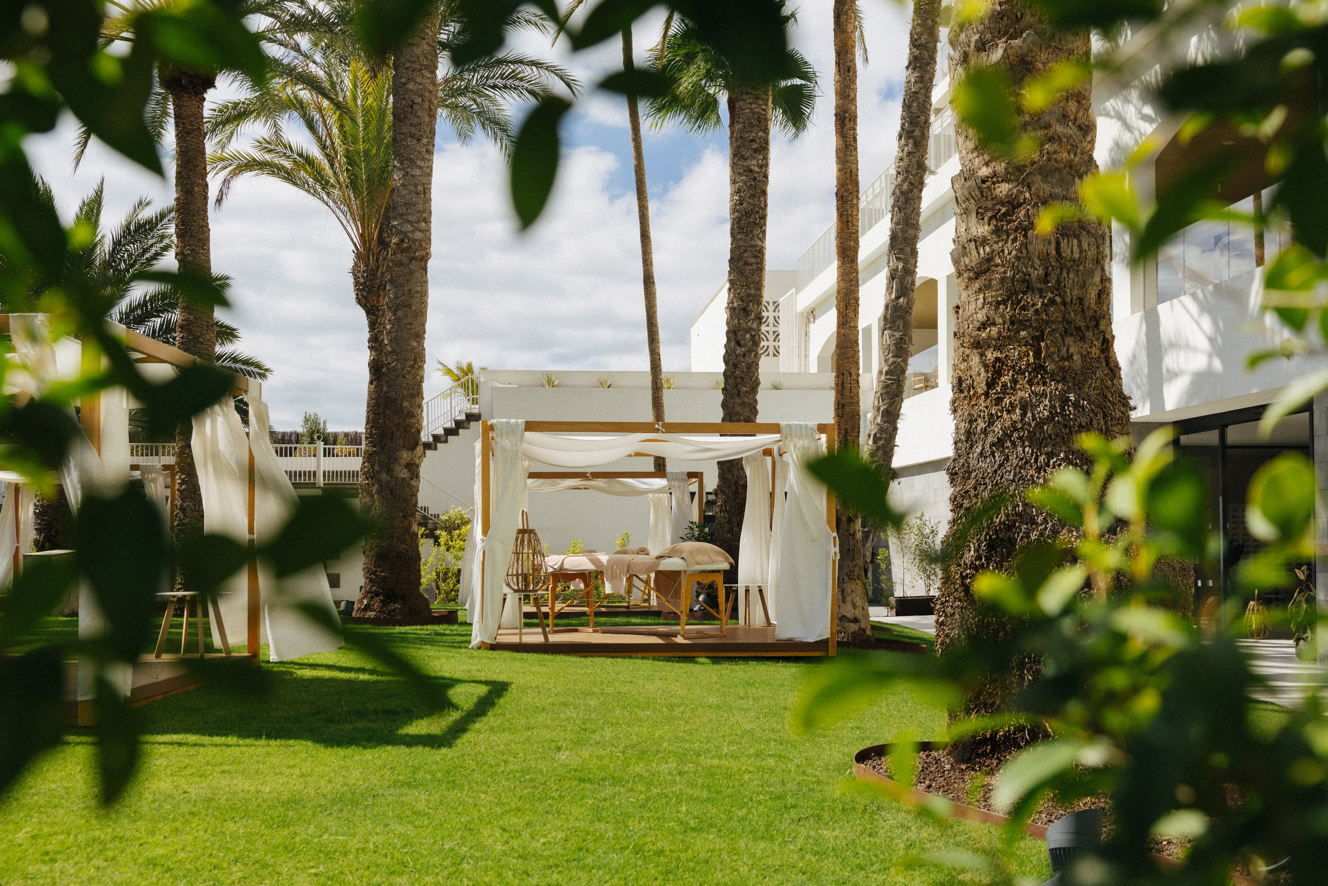 Outdoor spa cabana with massage tables, palm trees, and resort garden.
