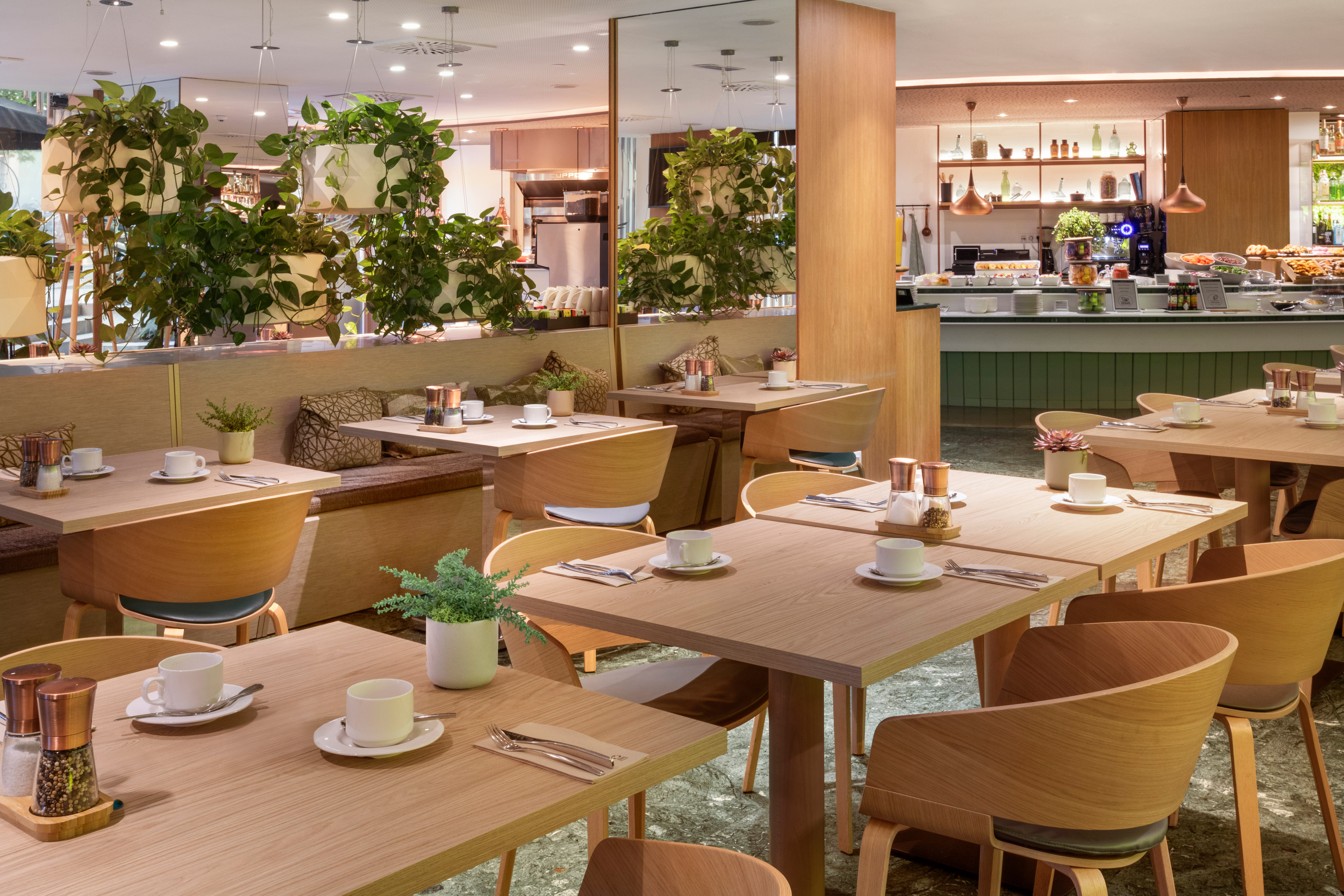 Modern restaurant with wooden tables, hanging plants, and buffet.