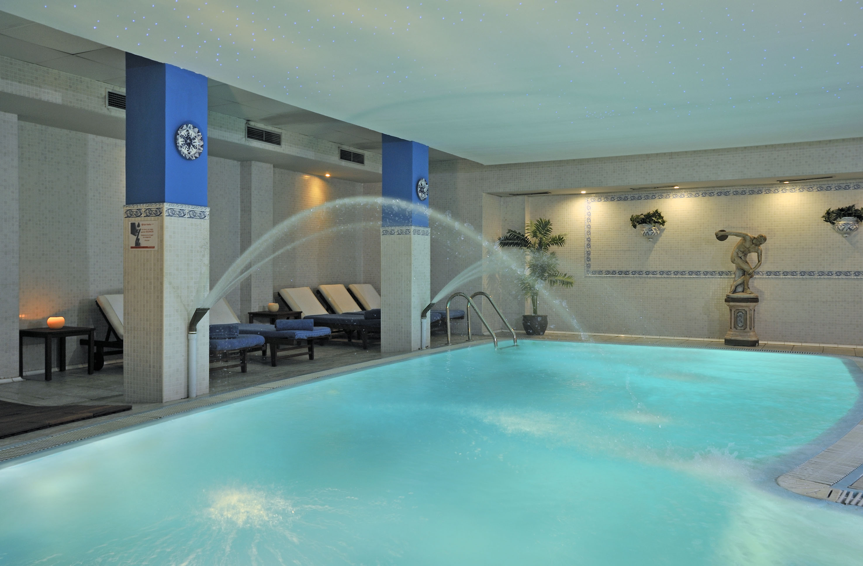 Indoor spa swimming pool with water jets, loungers, and star-lit ceiling.