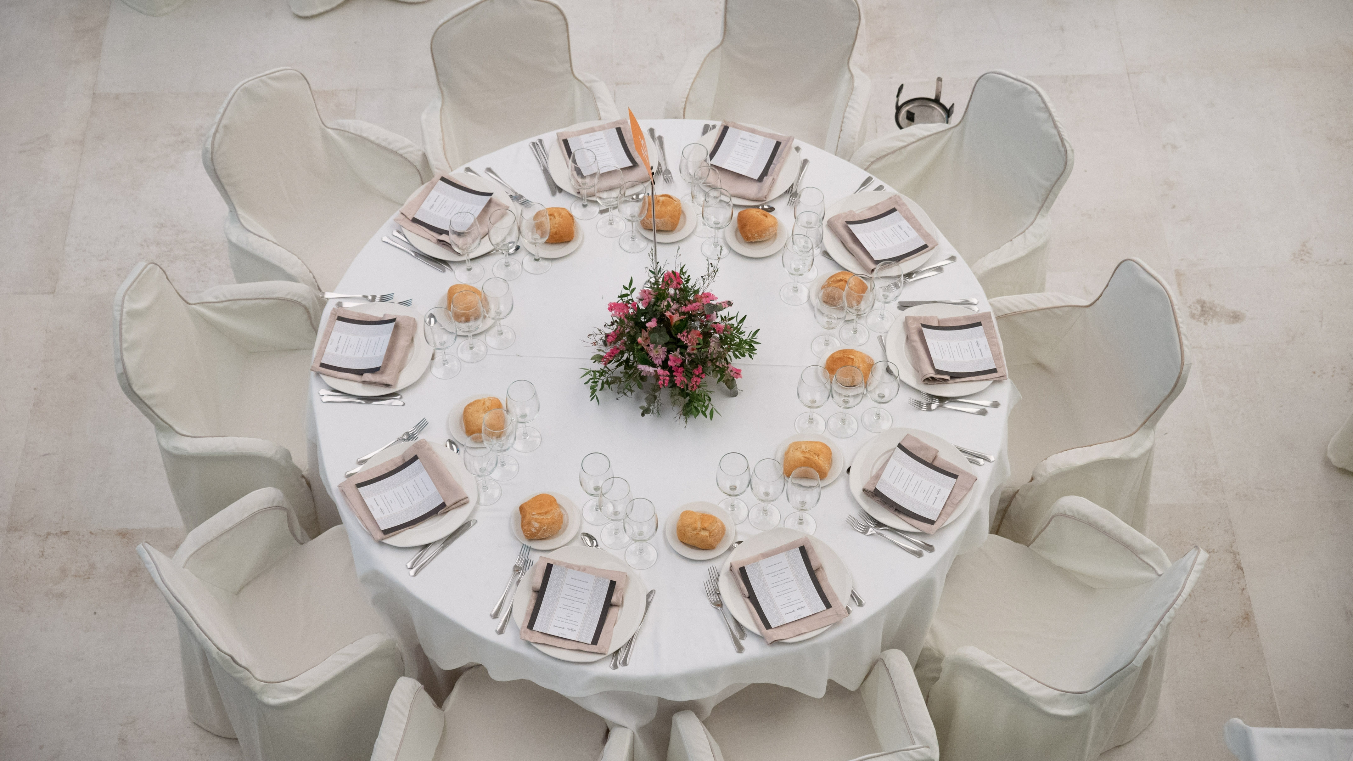 Round event table with white place settings, menus, and floral centerpiece.