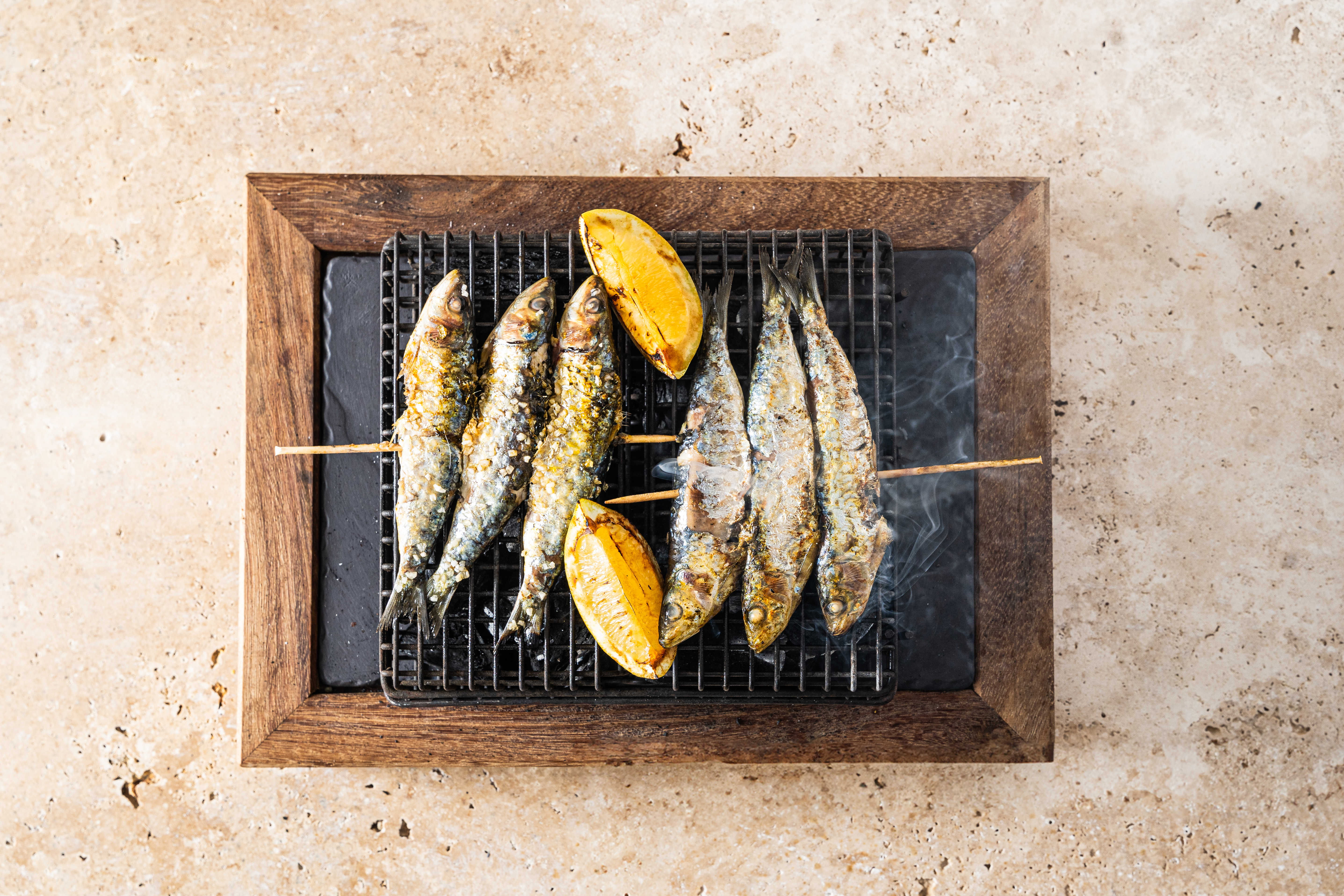 Sardinas asadas en brochetas con limón, humeando en una parrilla.