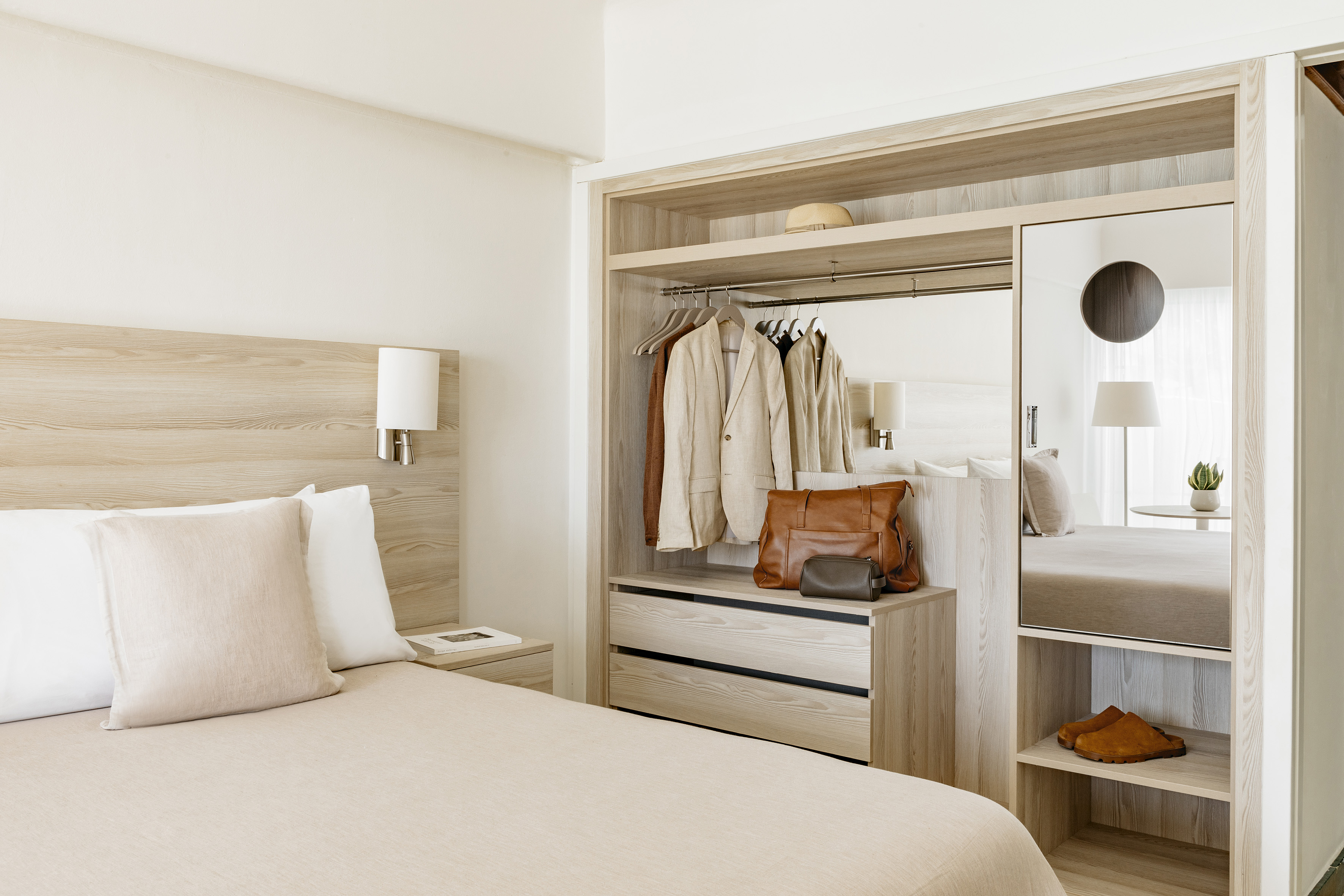 Modern hotel bedroom with integrated light wood wardrobe and neutral decor.