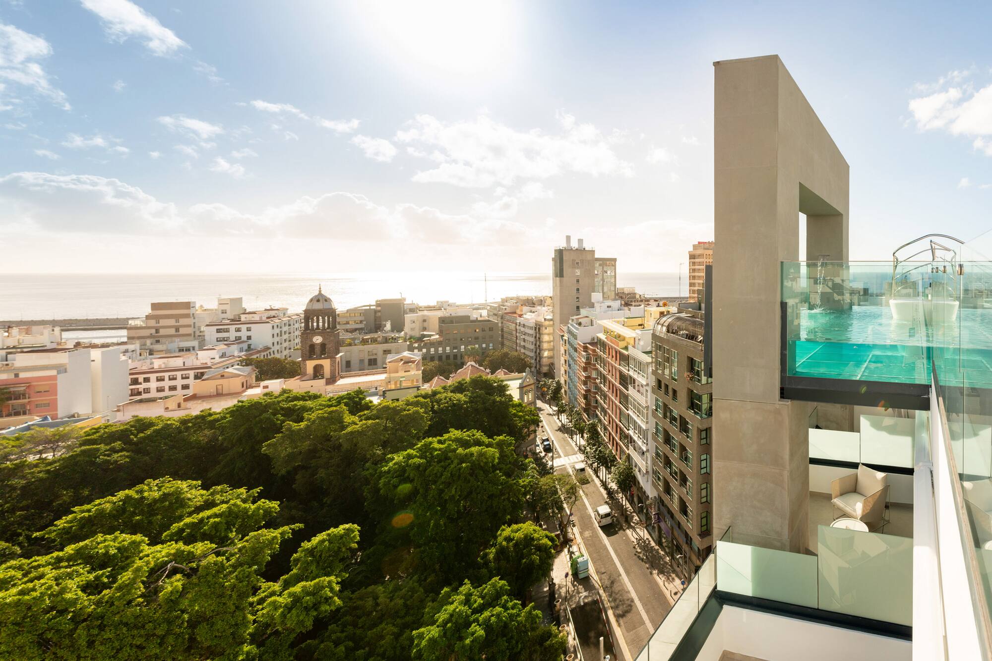 Modern rooftop pool overlooking a sunny city, ocean, and green park.