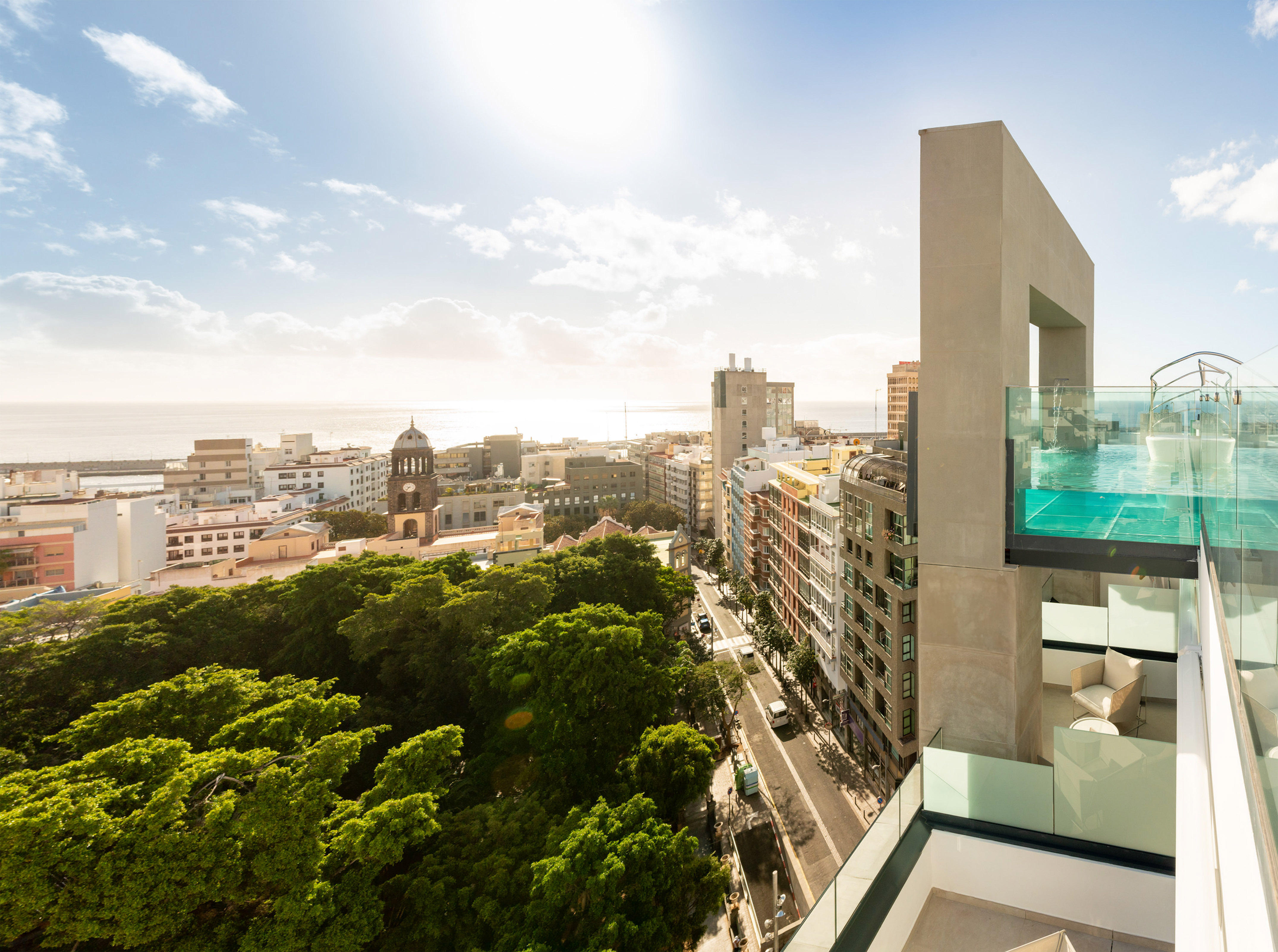 Modern rooftop pool overlooking a sunny city, ocean, and green park.
