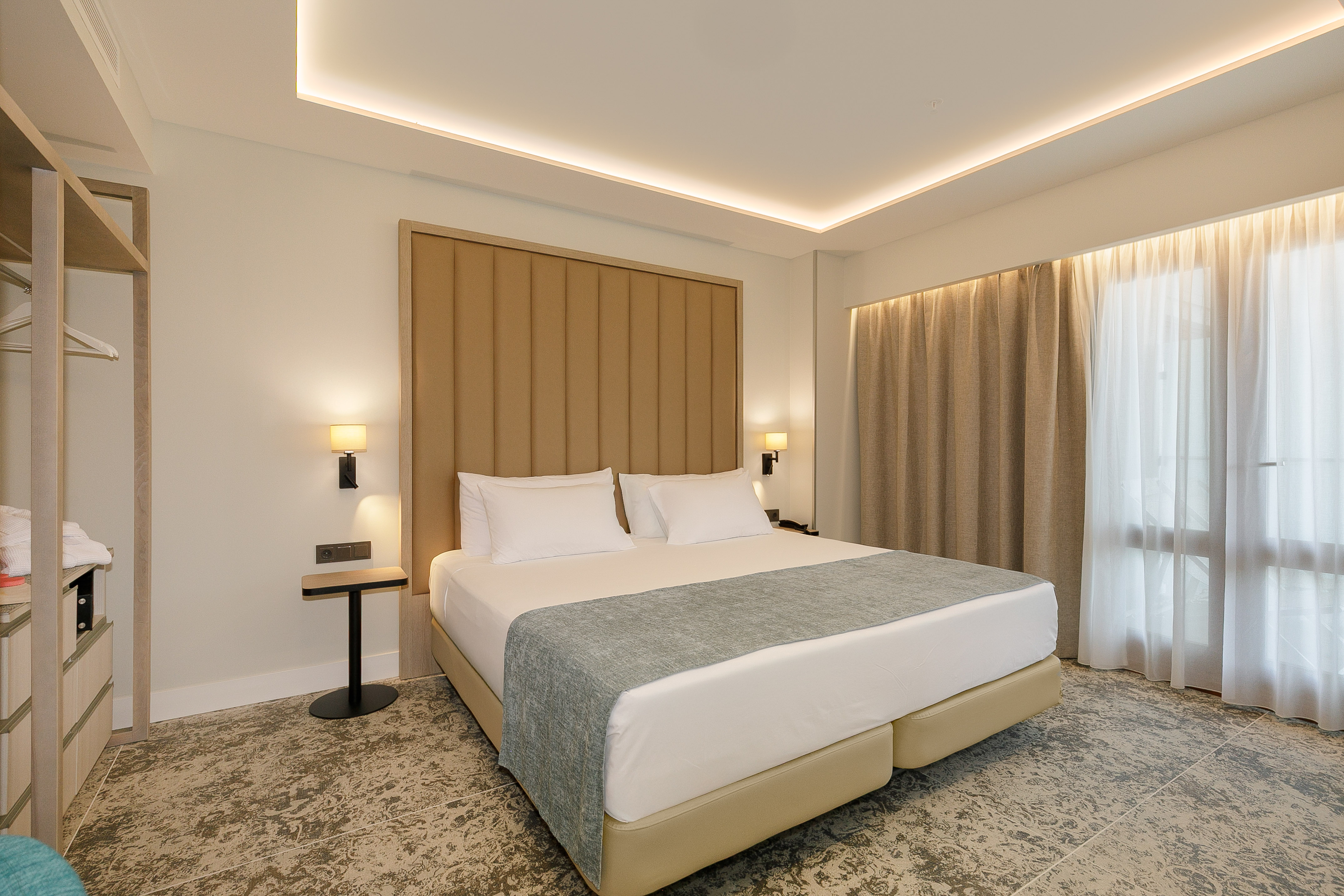 Modern hotel bedroom with large bed, padded headboard, and ambient lighting.