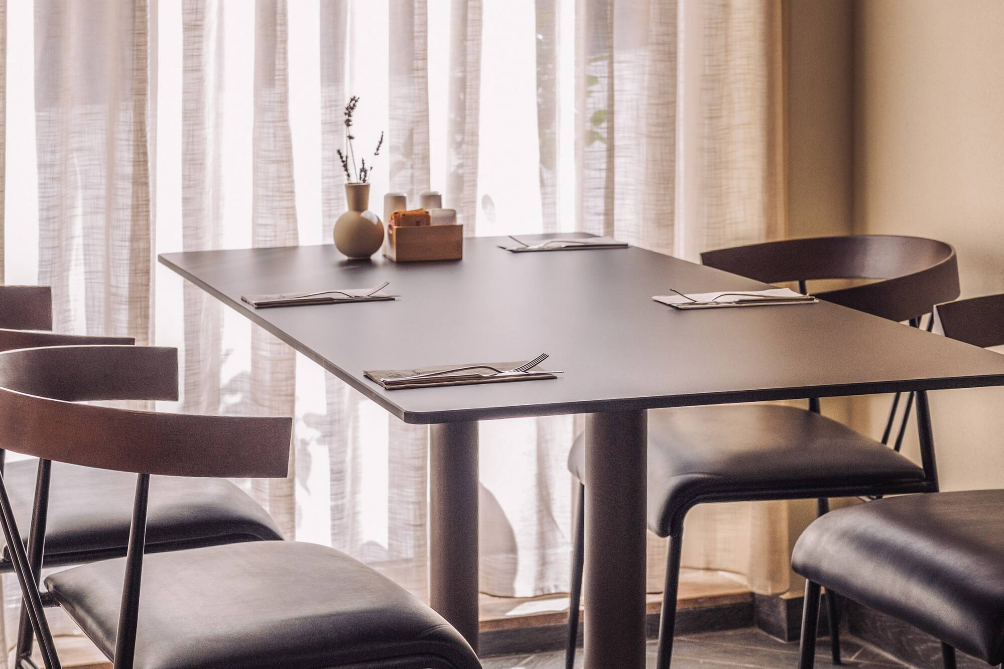 Modern cafe dining table with four chairs, place settings, and bright window.