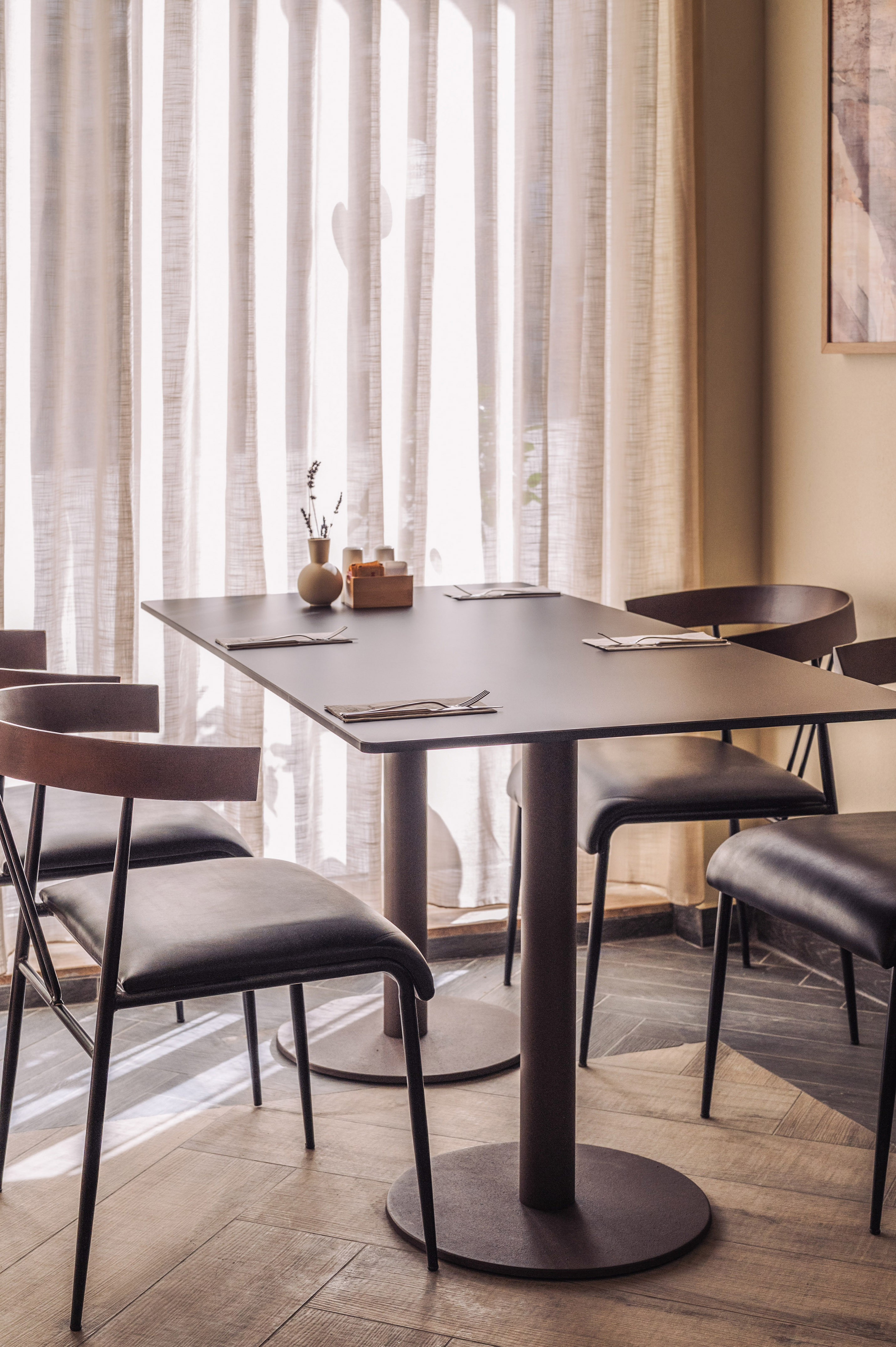 Modern cafe dining table with four chairs, place settings, and bright window.