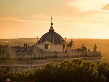 Royal Palace of Madrid dome at golden sunset, trees in foreground.