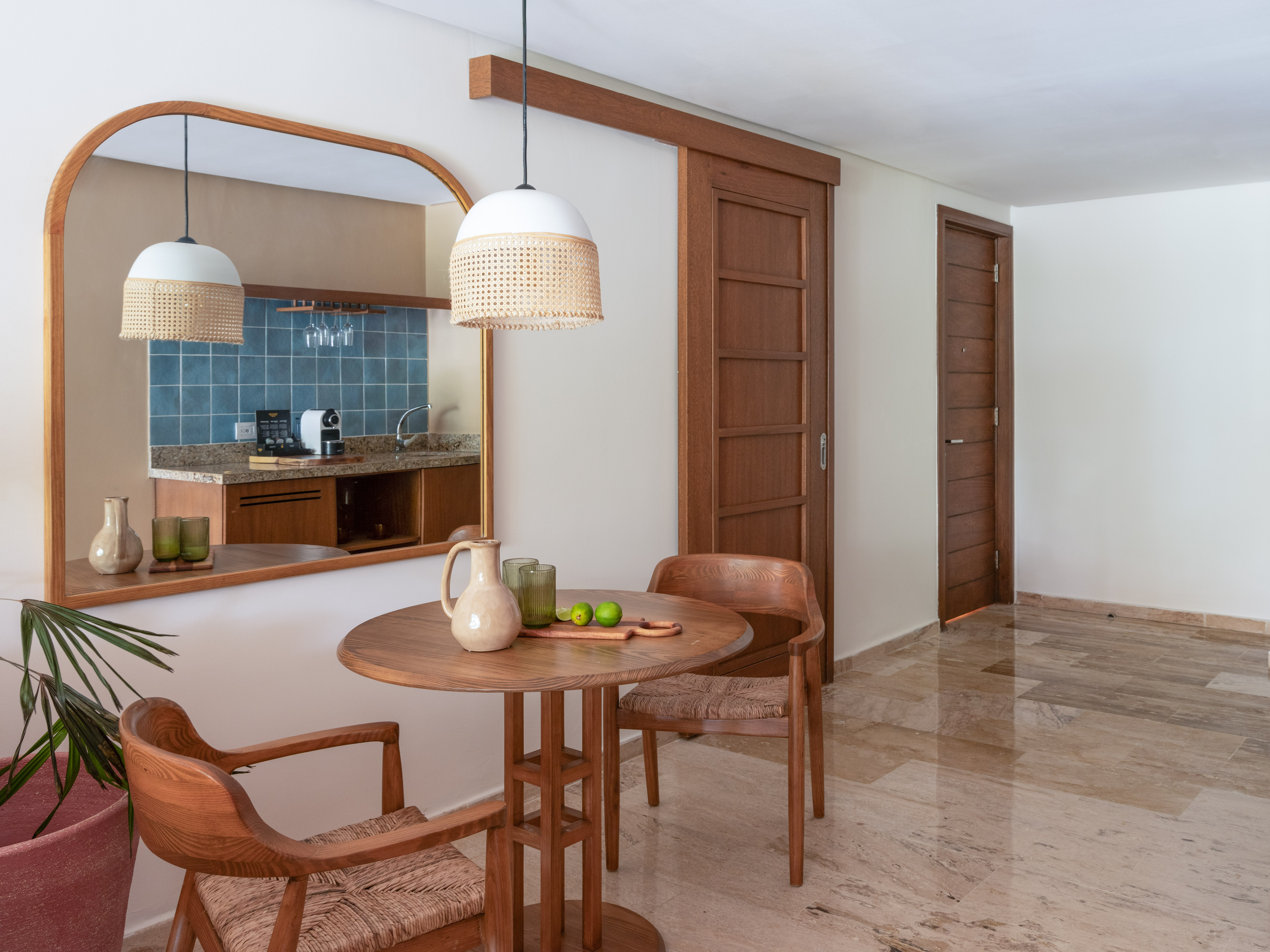 Modern dining area with wooden table, rattan pendant light, reflected kitchen.