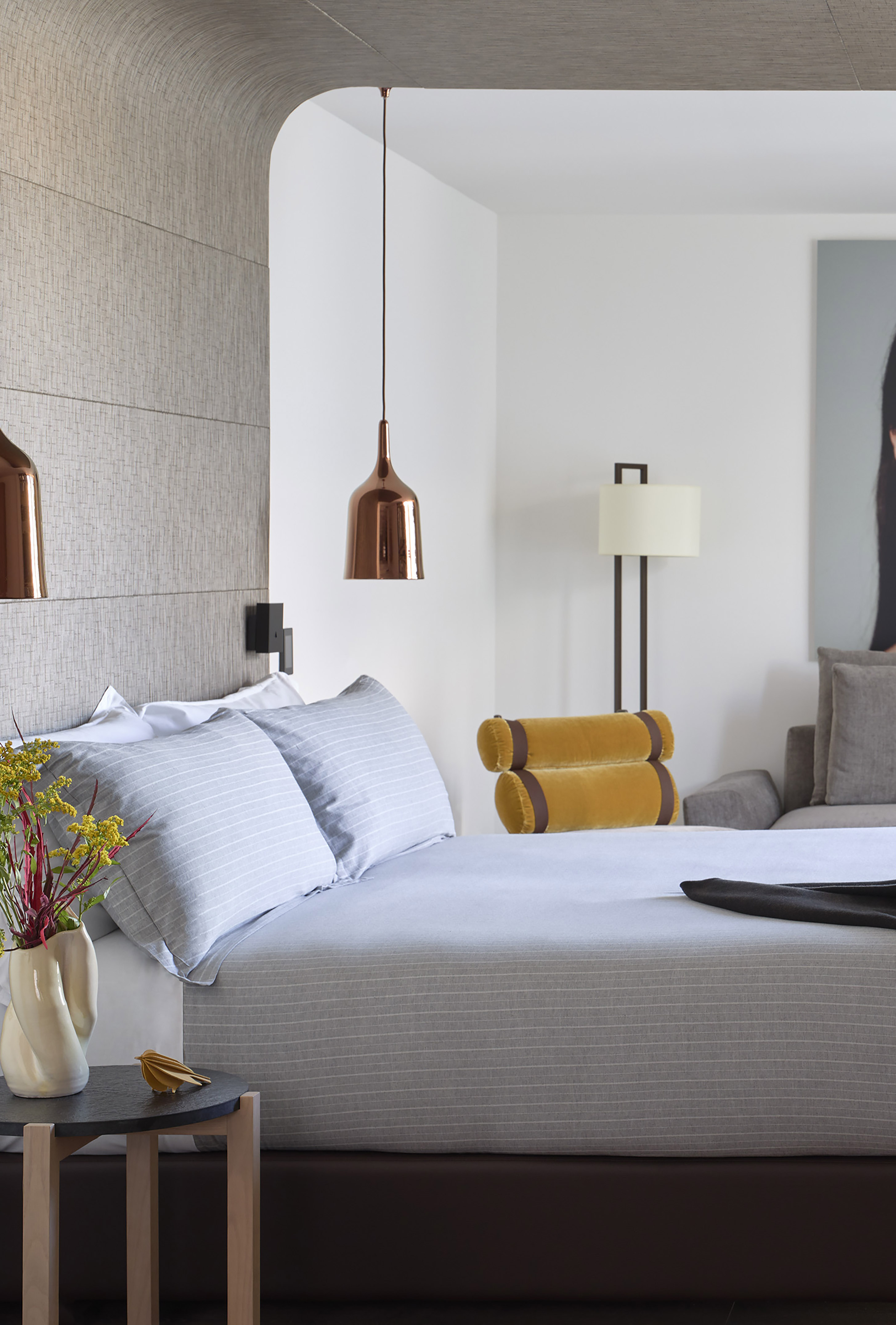Modern bedroom with striped bed, copper pendant lights, and textured arched wall.