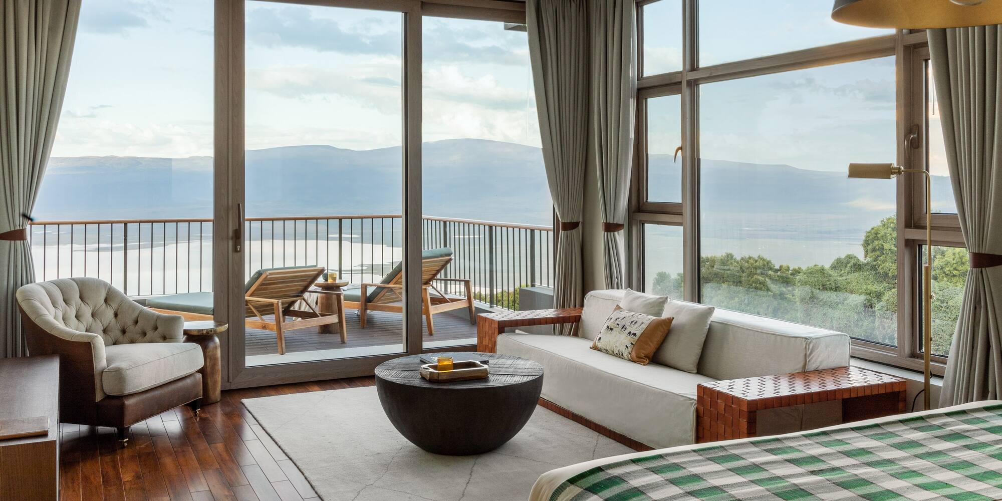 Modern hotel suite with balcony overlooking lake and mountains.