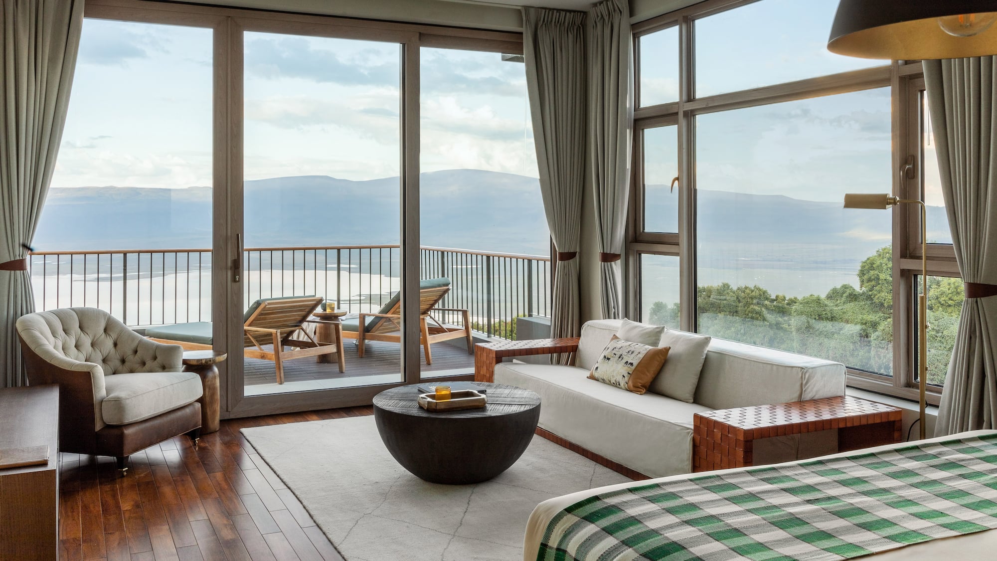 Modern hotel suite with balcony overlooking lake and mountains.