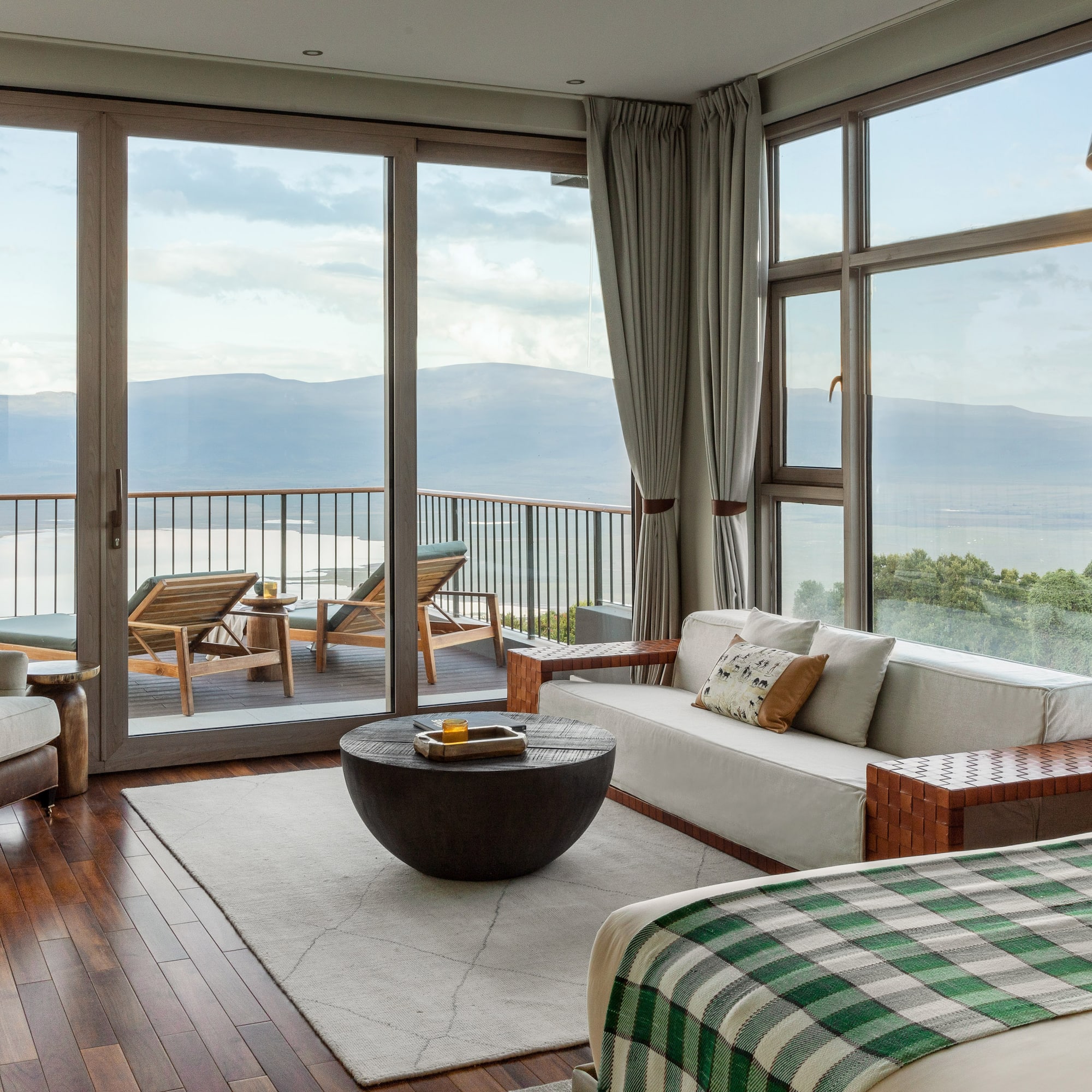 Modern hotel suite with balcony overlooking lake and mountains.