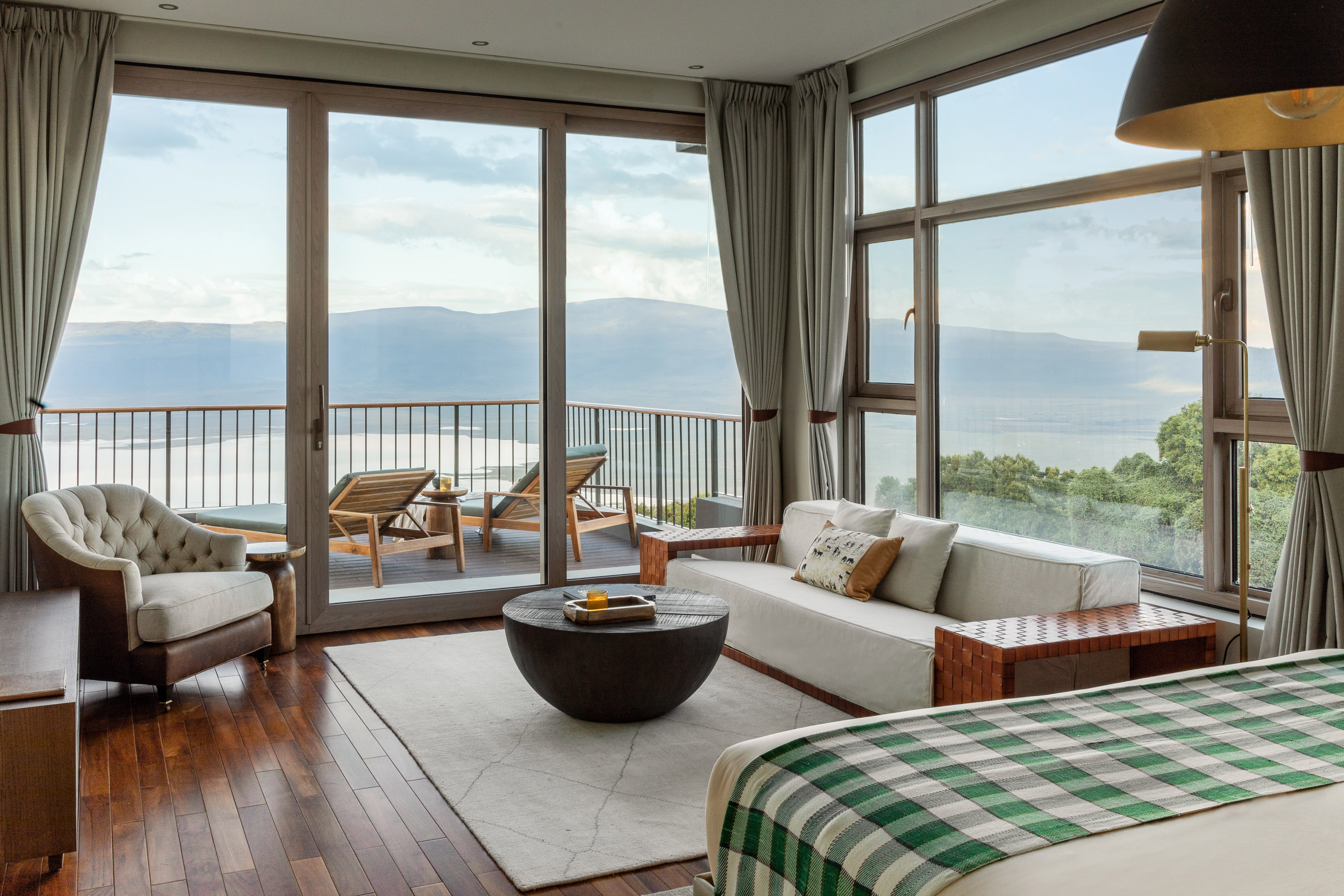 Modern hotel suite with balcony overlooking lake and mountains.