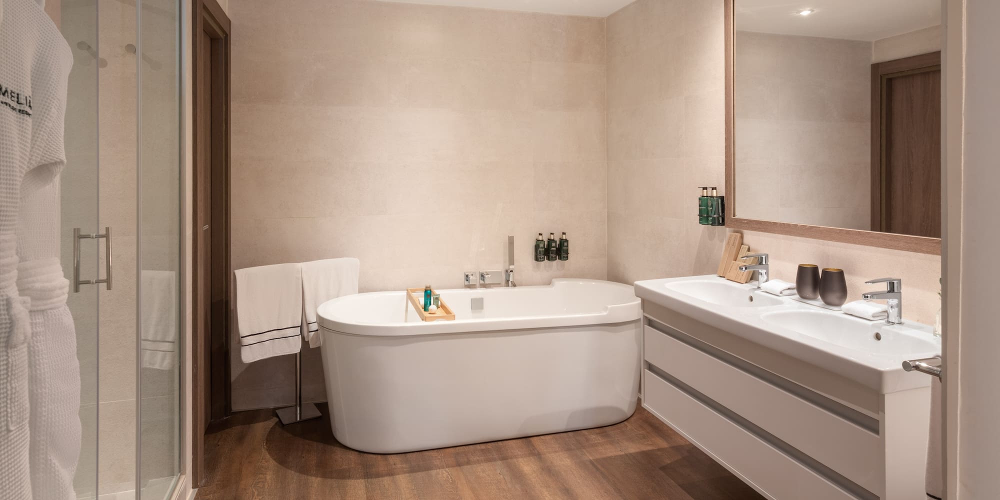 Luxury hotel bathroom with white tub, glass shower, and dual vanity.