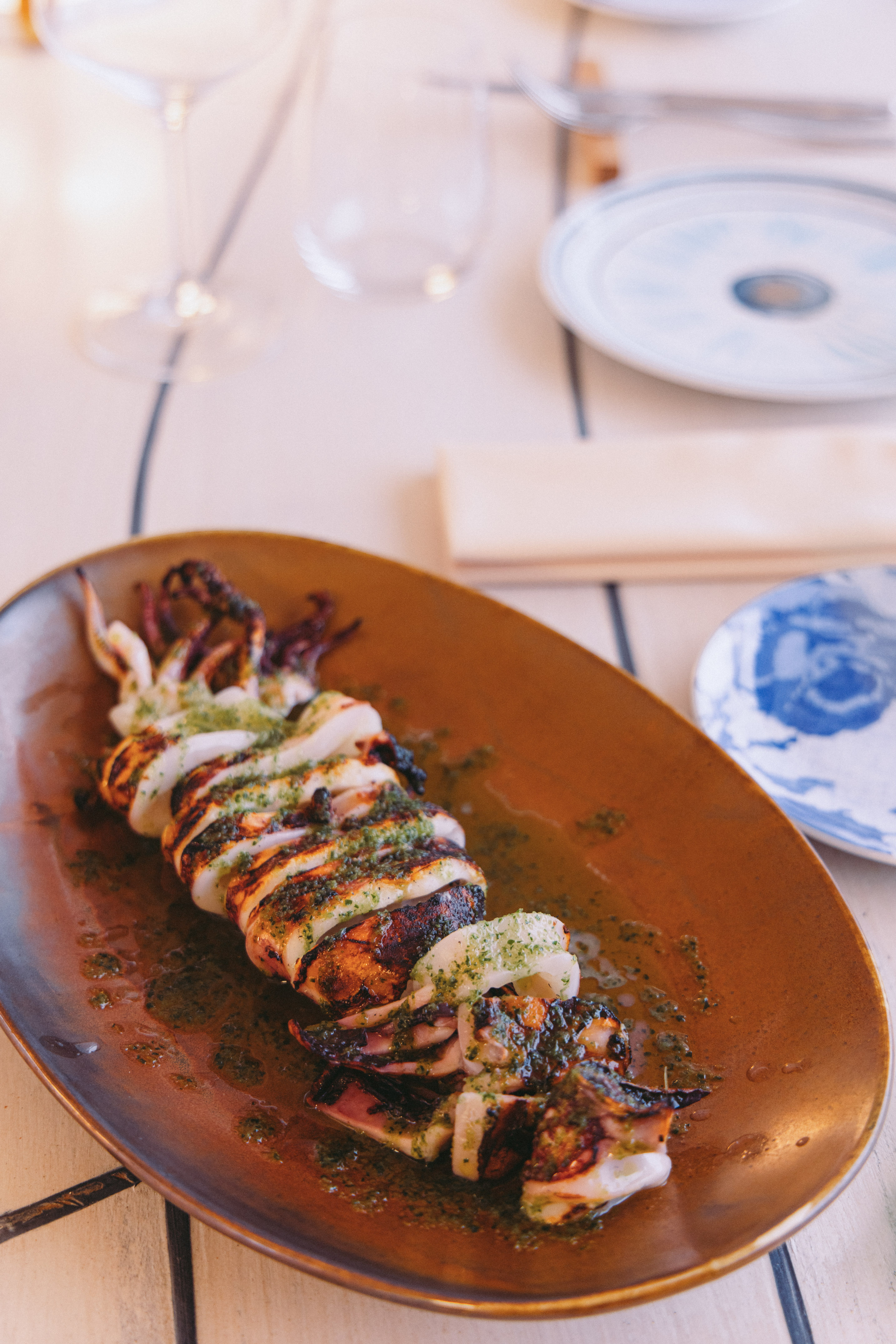 Grilled squid with green herb sauce on a brown plate at a restaurant.