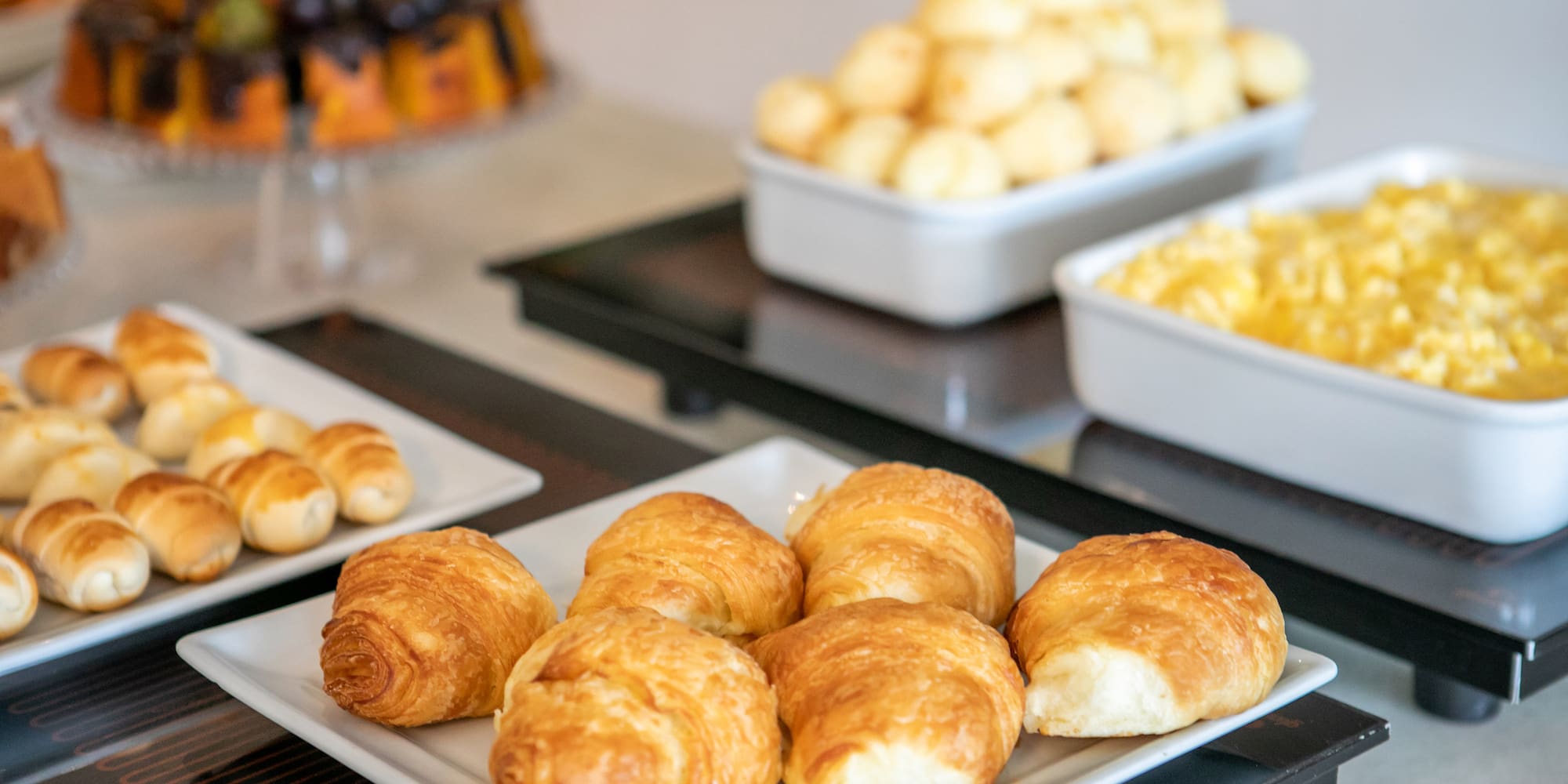 Fresh croissants, pastries, scrambled eggs, and cheese balls on a breakfast buffet.