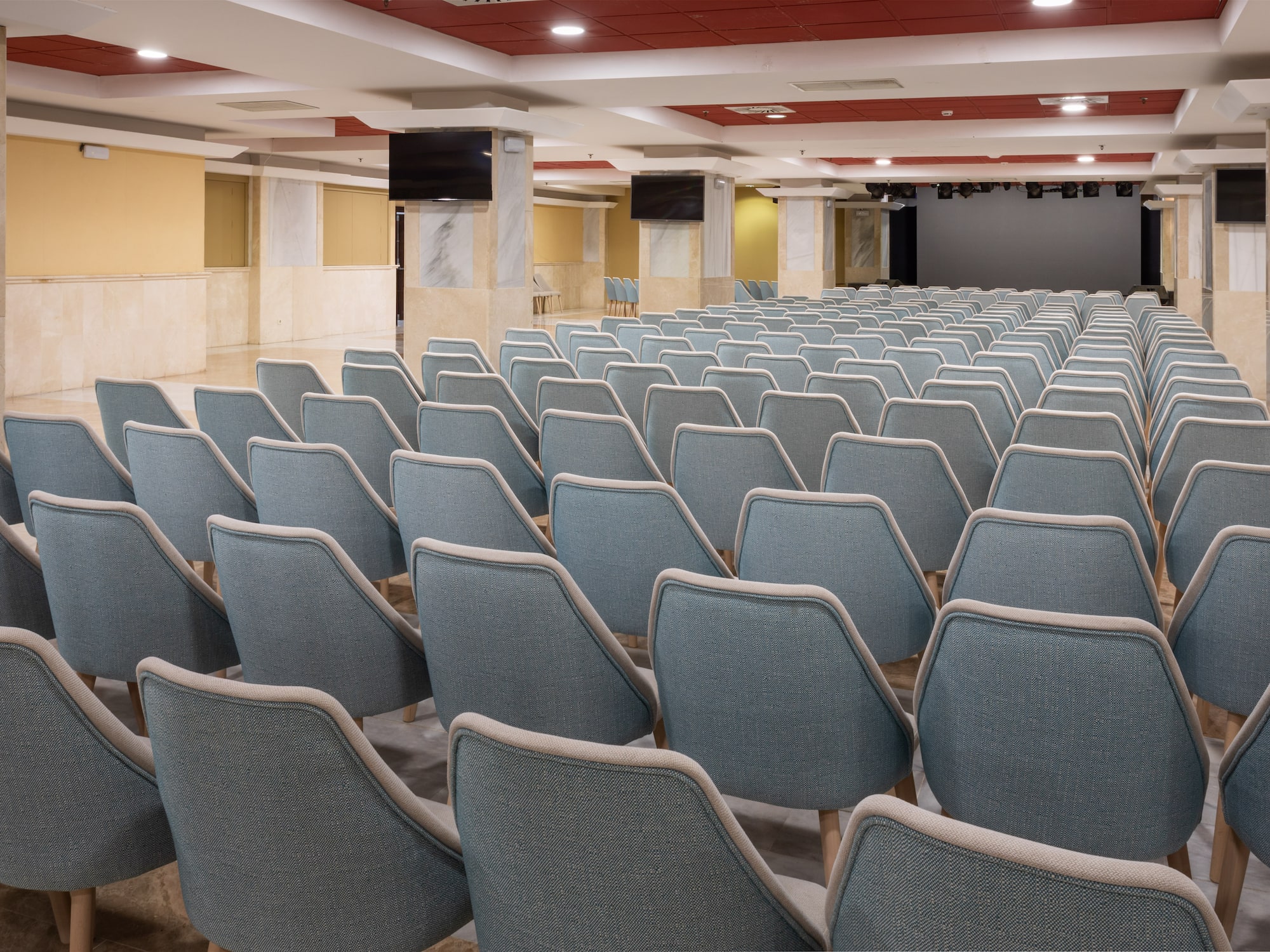 Empty conference room with blue chairs, stage, and monitors