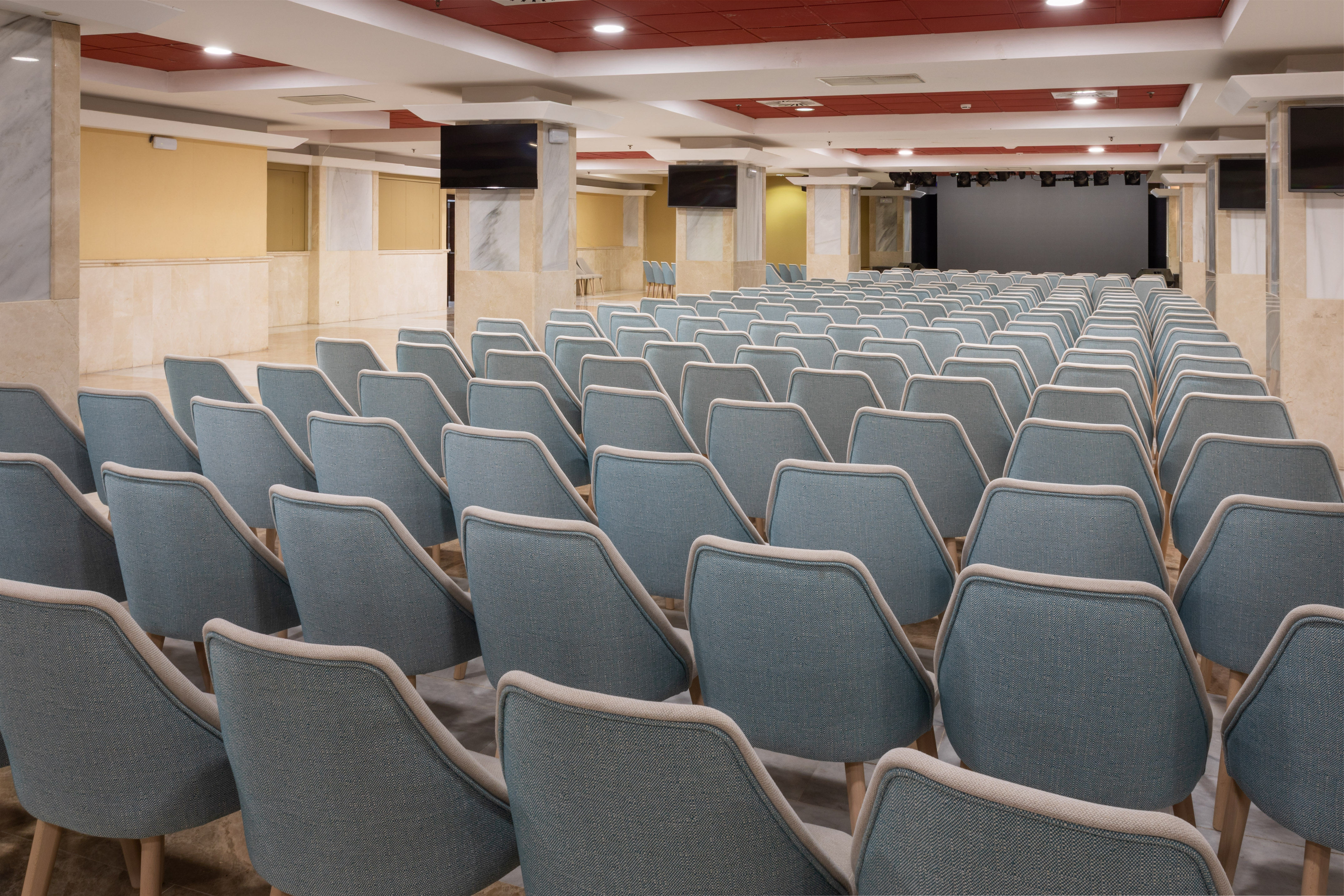 Empty conference room with blue chairs, stage, and monitors