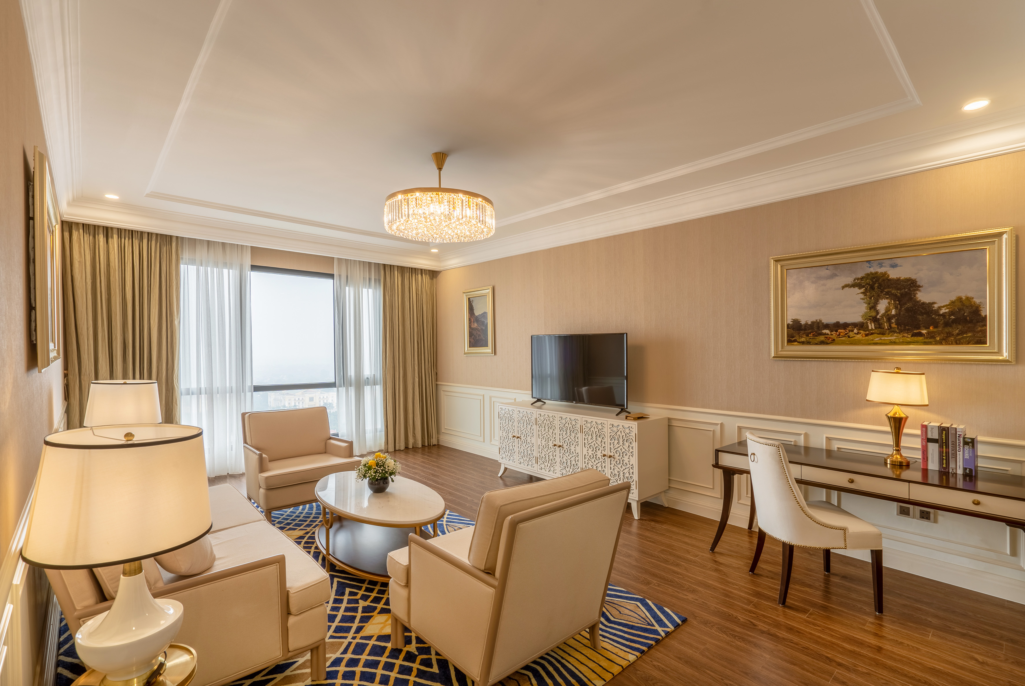 Elegant hotel suite living room with neutral furniture, TV, and large window.