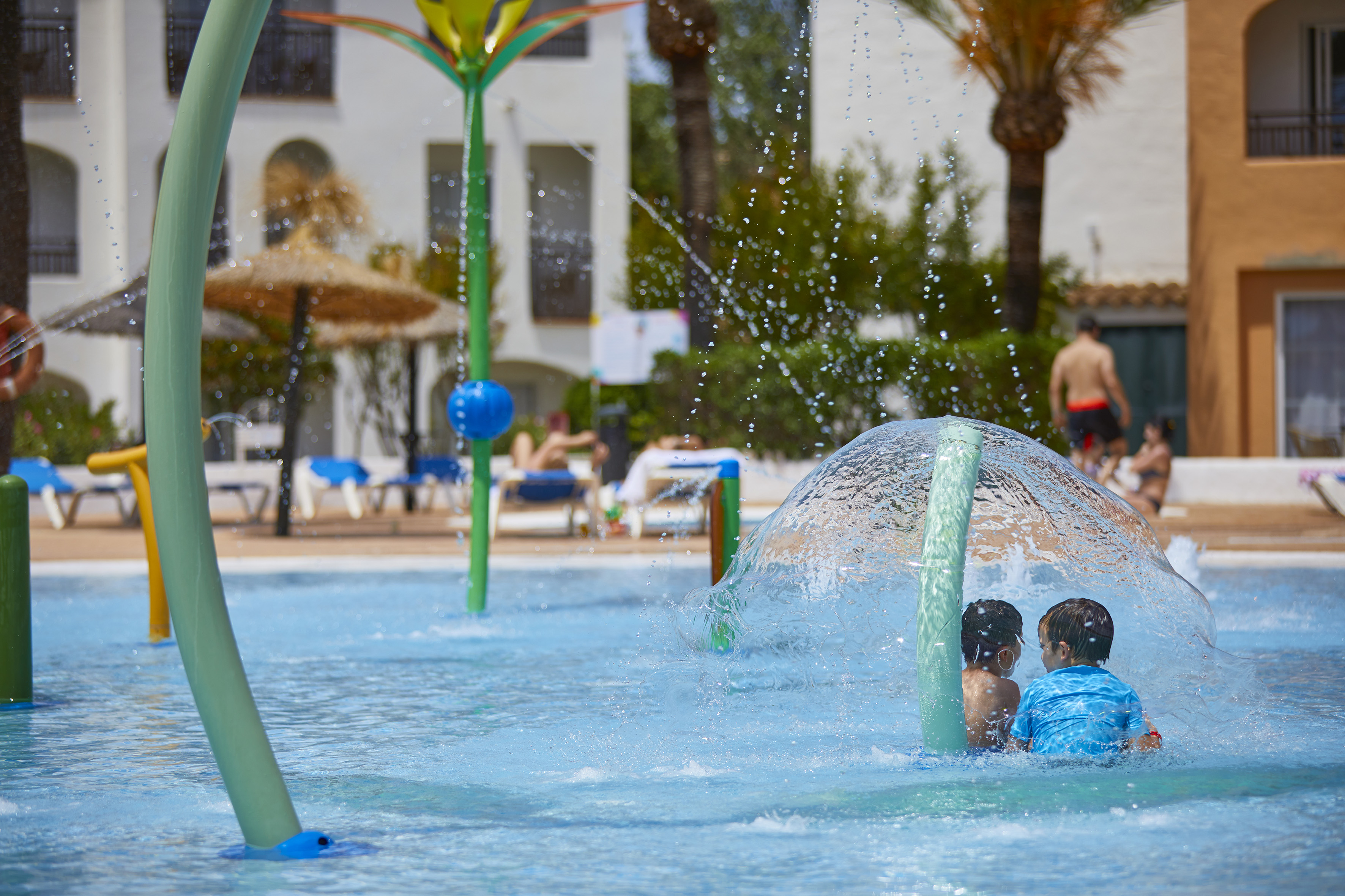 Children playing in resort splash pool with water fountain.