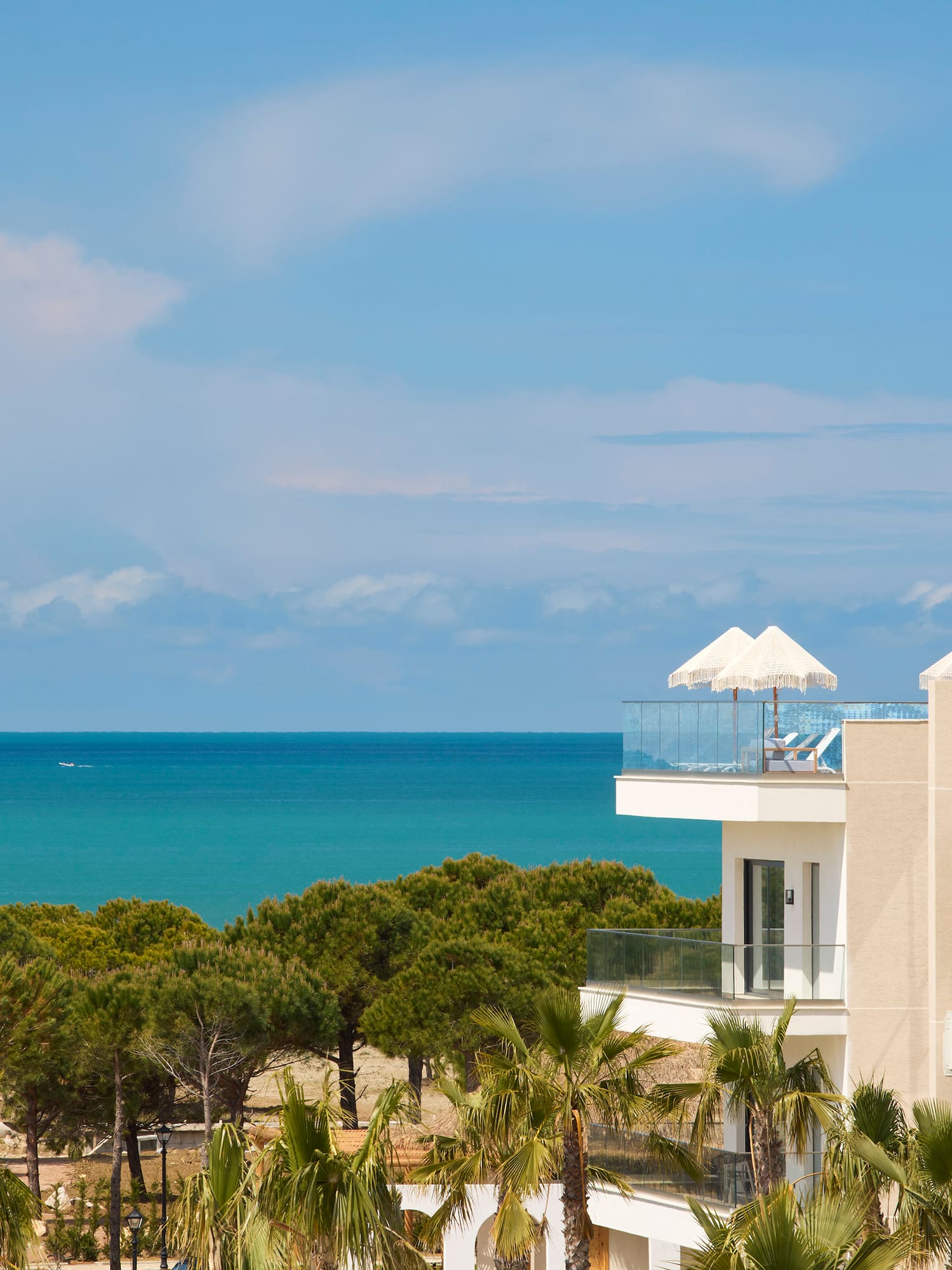 Hotel resort moderno con balcón al mar, palmeras y sombrillas.