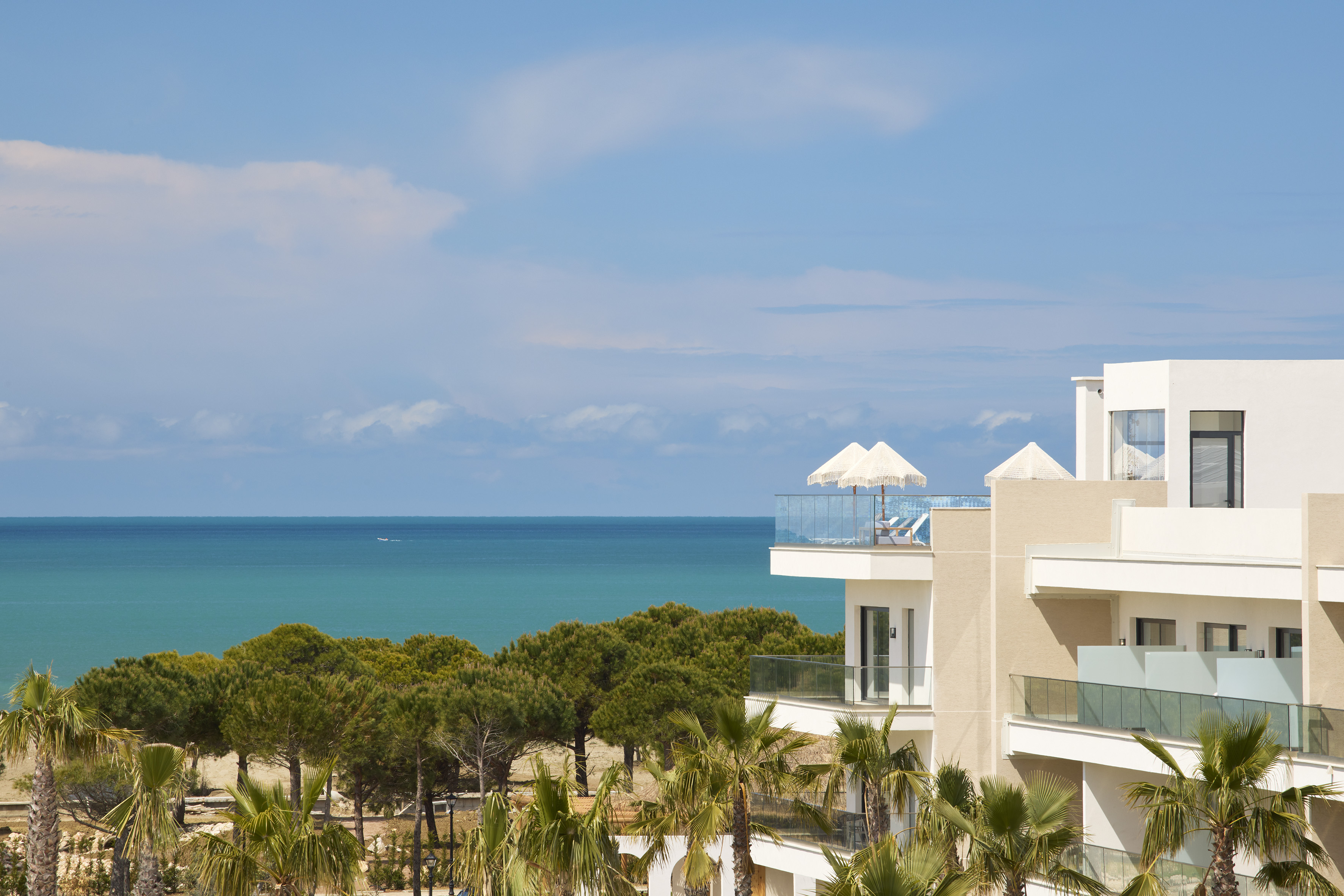 Hotel resort moderno con balcón al mar, palmeras y sombrillas.