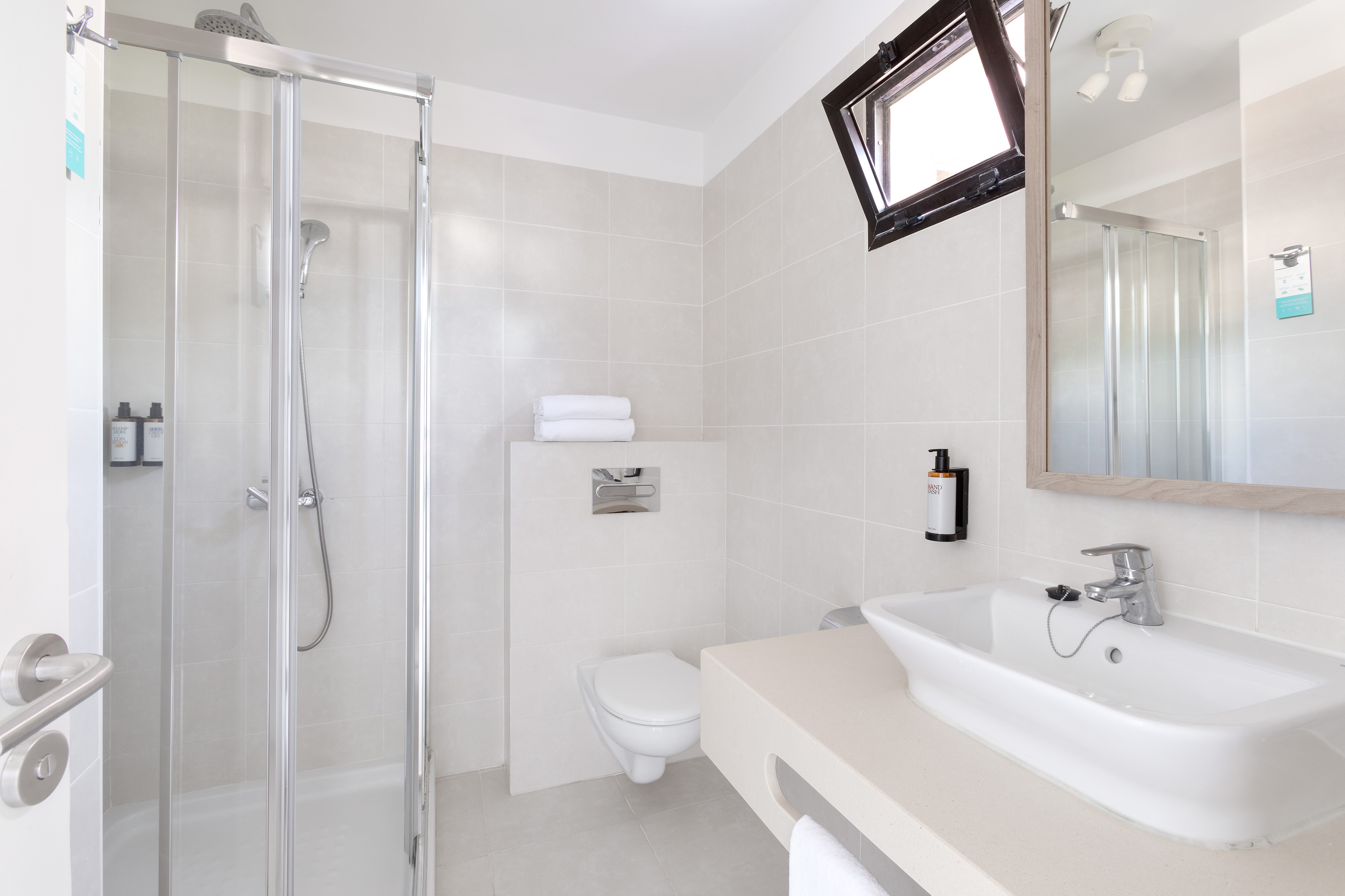 Modern hotel bathroom with shower, white toilet, sink, and large mirror.