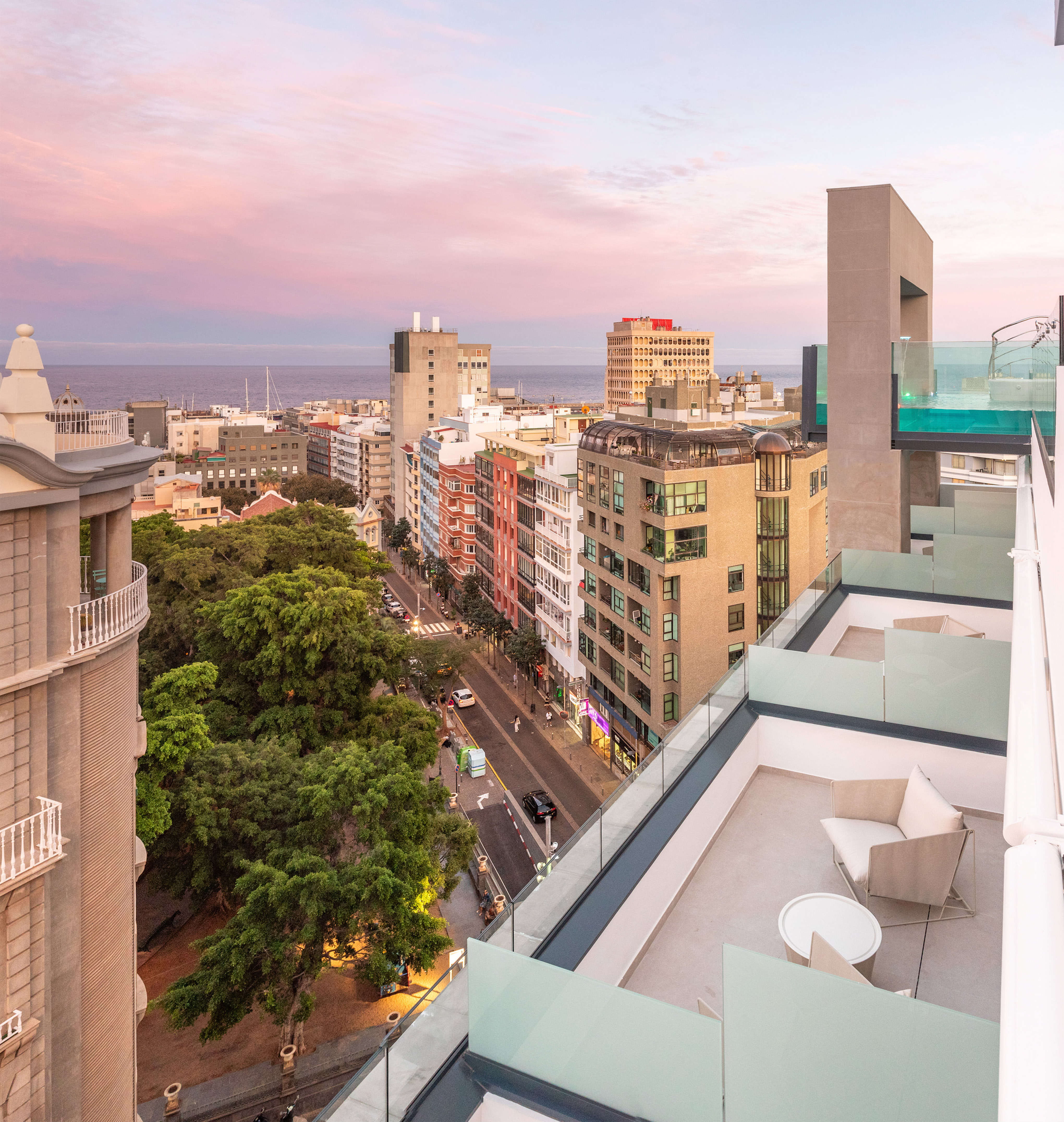 Sunset cityscape over ocean from a modern rooftop with a pool terrace.