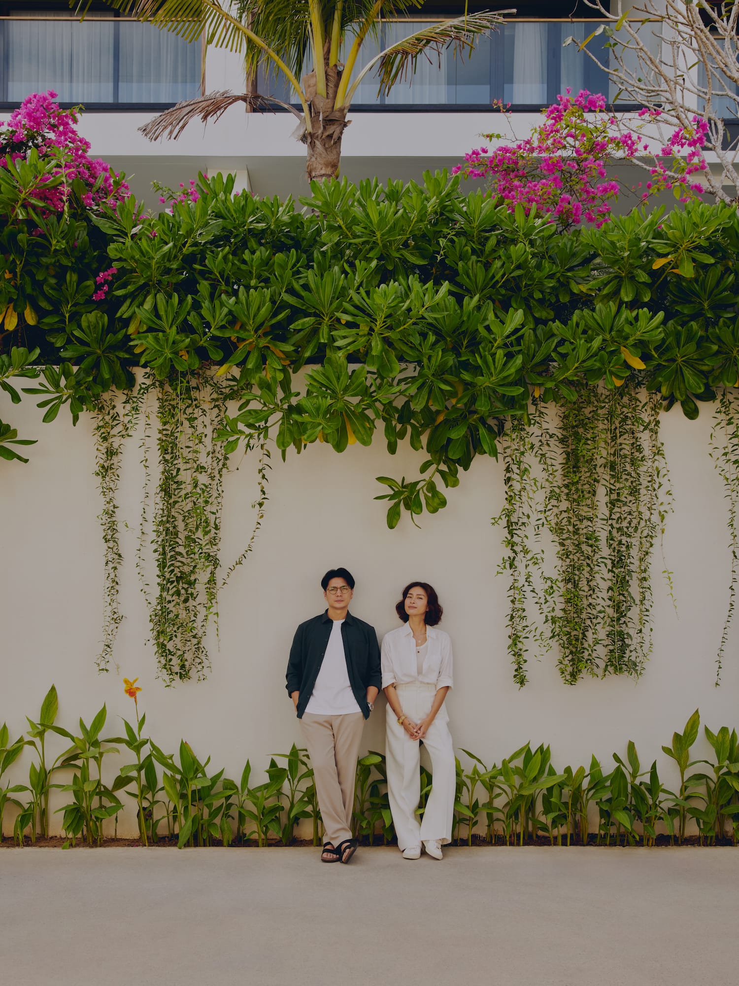a man and woman standing in front of a wall with plants and trees