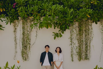 a man and woman standing in front of a wall with plants and trees