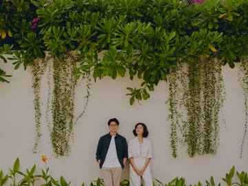 a man and woman standing in front of a wall with plants and trees