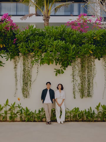 a man and woman standing in front of a wall with plants and trees