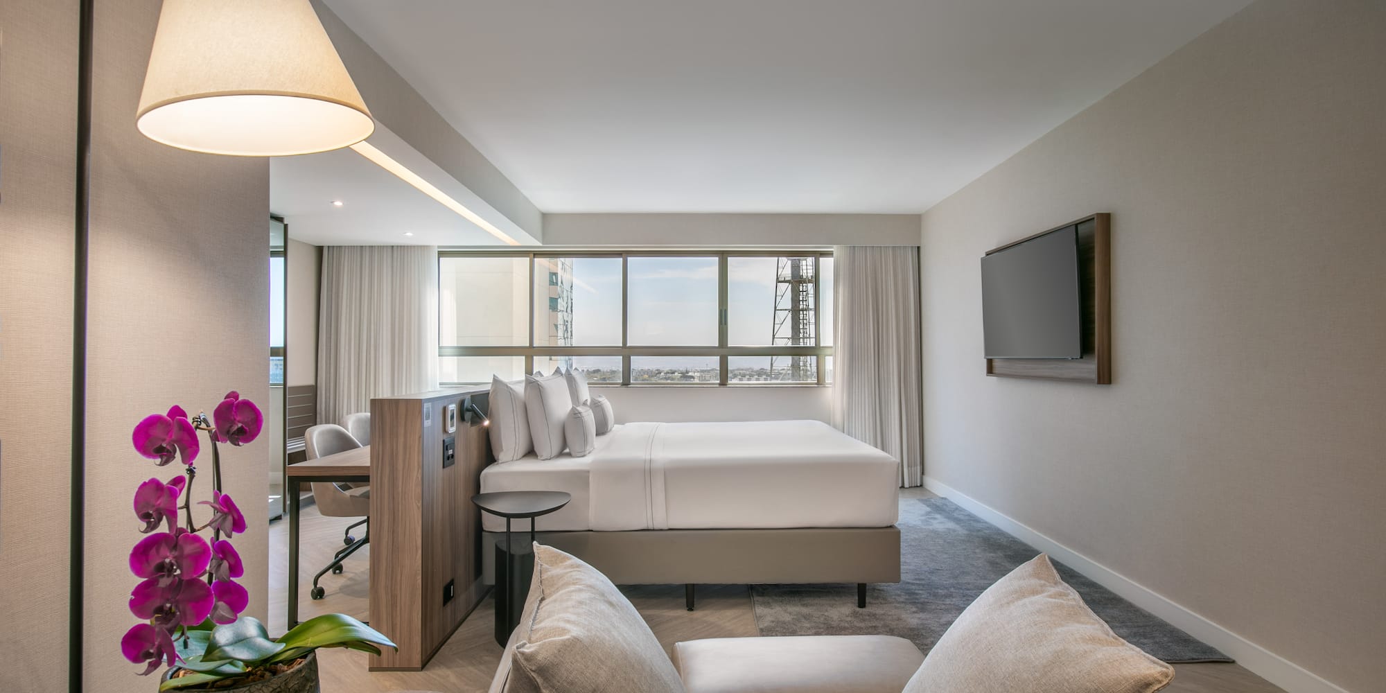 Modern hotel suite with king bed, city view, living area, and desk.