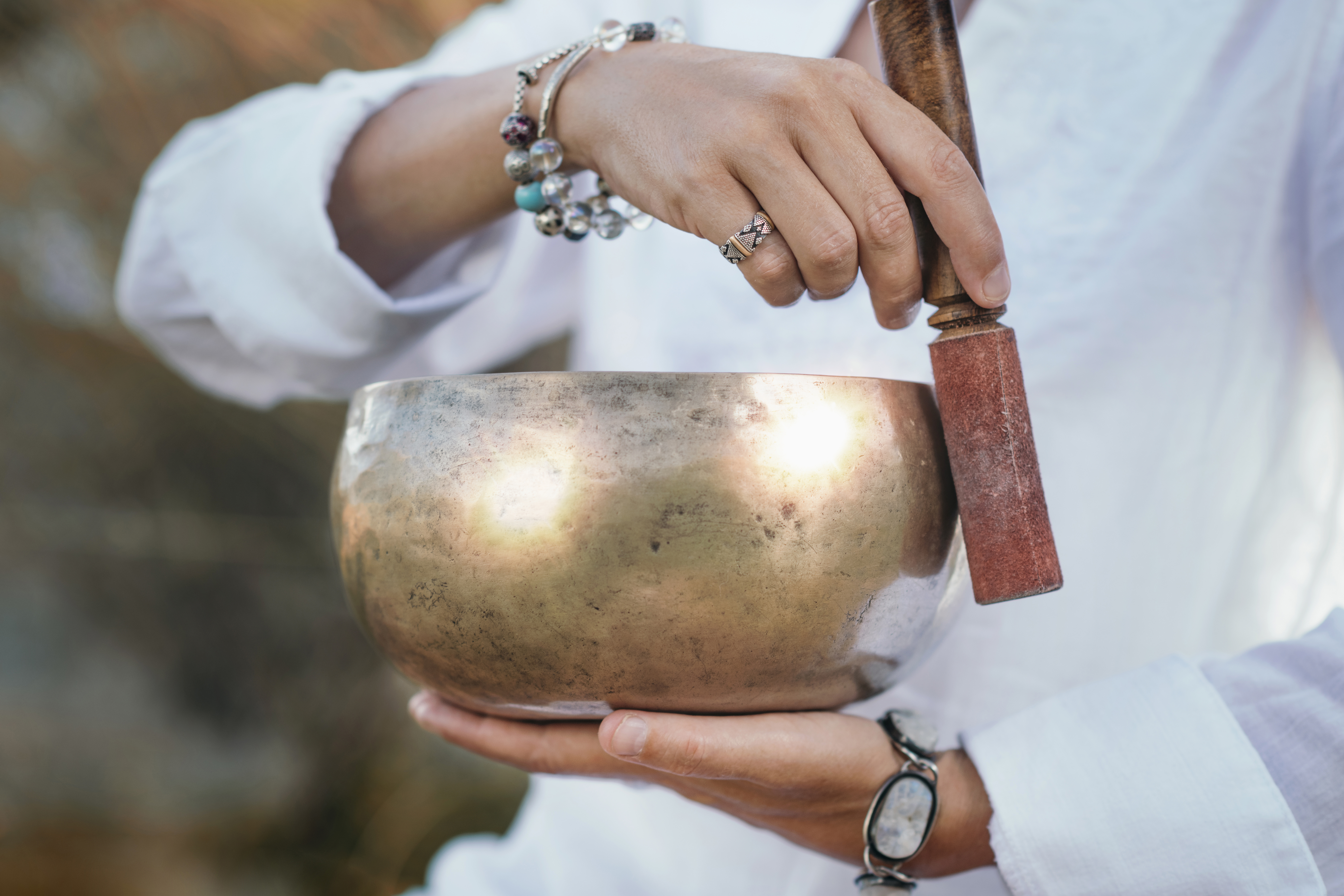 Hands playing bronze singing bowl with mallet for meditation or sound therapy.