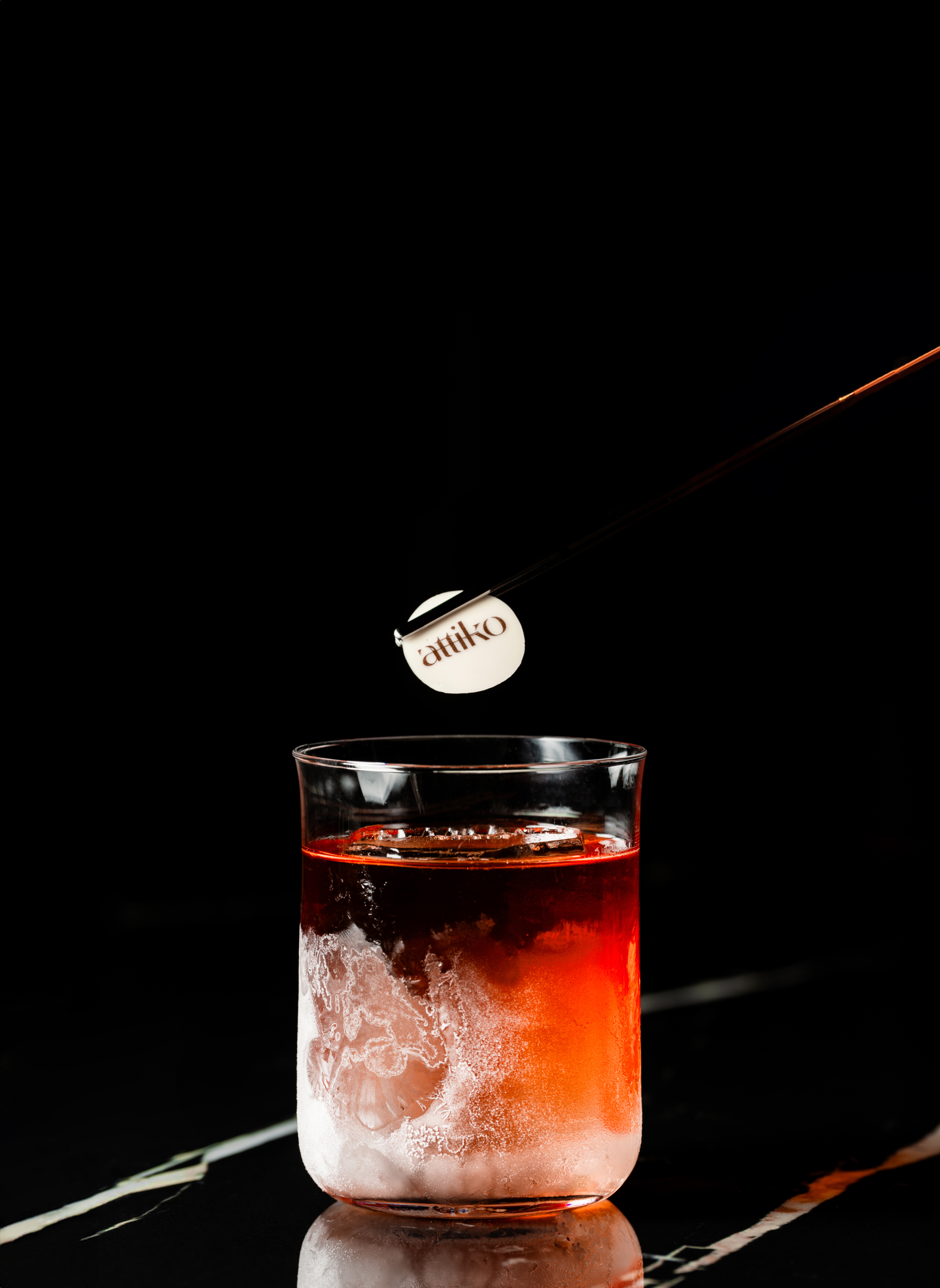 Attiko cocktail with large ice and frosted glass on a dark background.