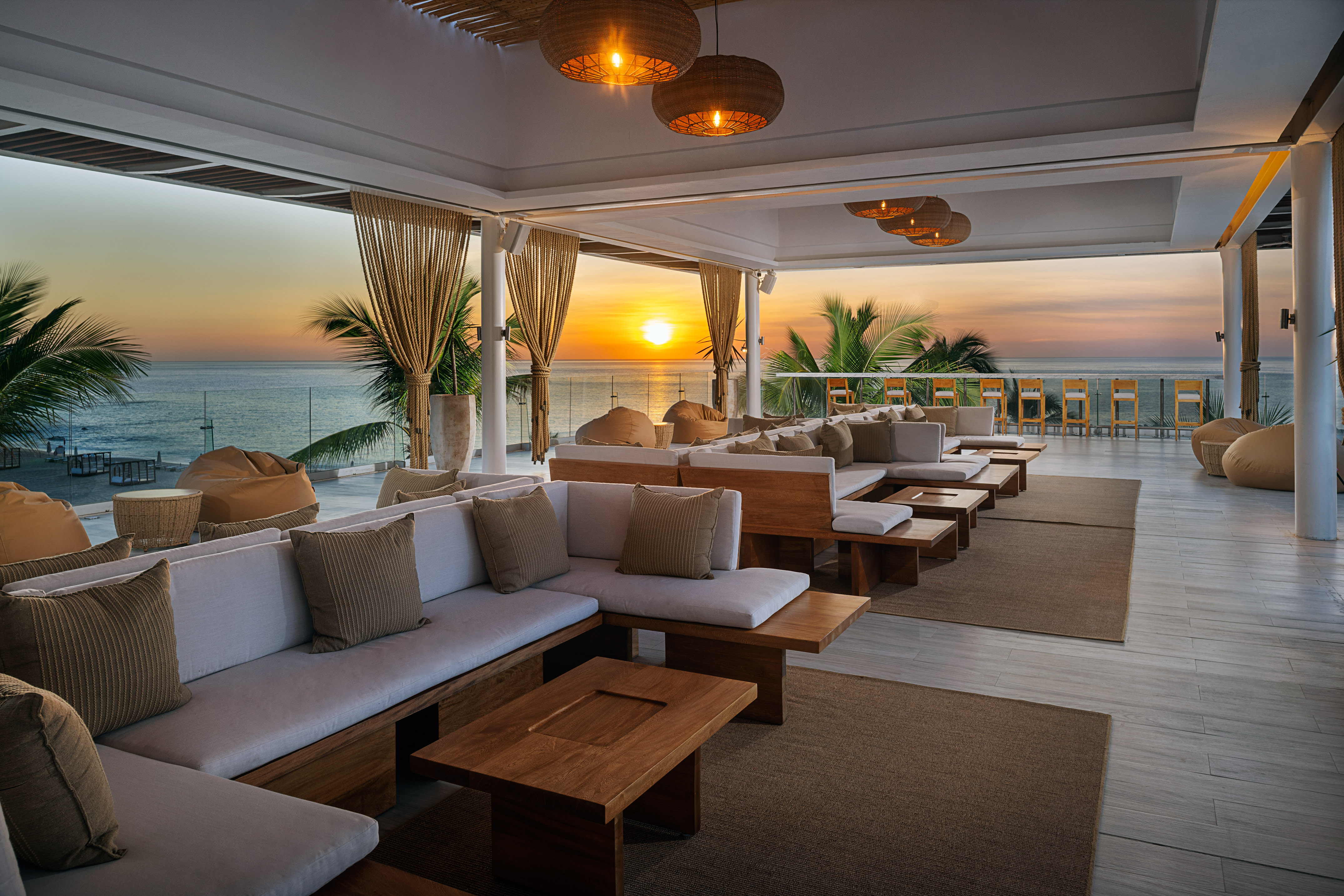 Oceanfront lounge terrace at sunset with comfortable seating and palm trees.