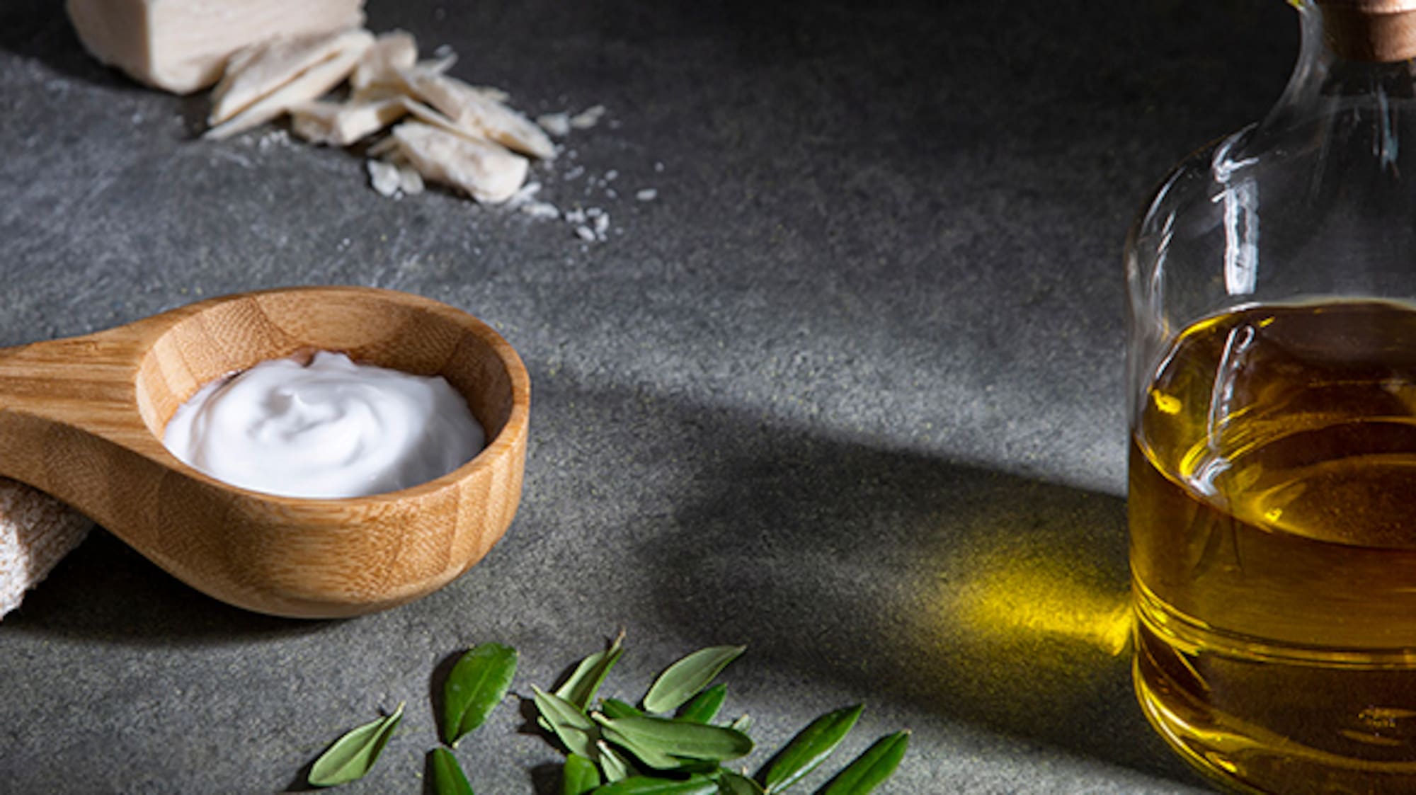 a spoon with a wooden spoon next to a bottle of oil and leaves